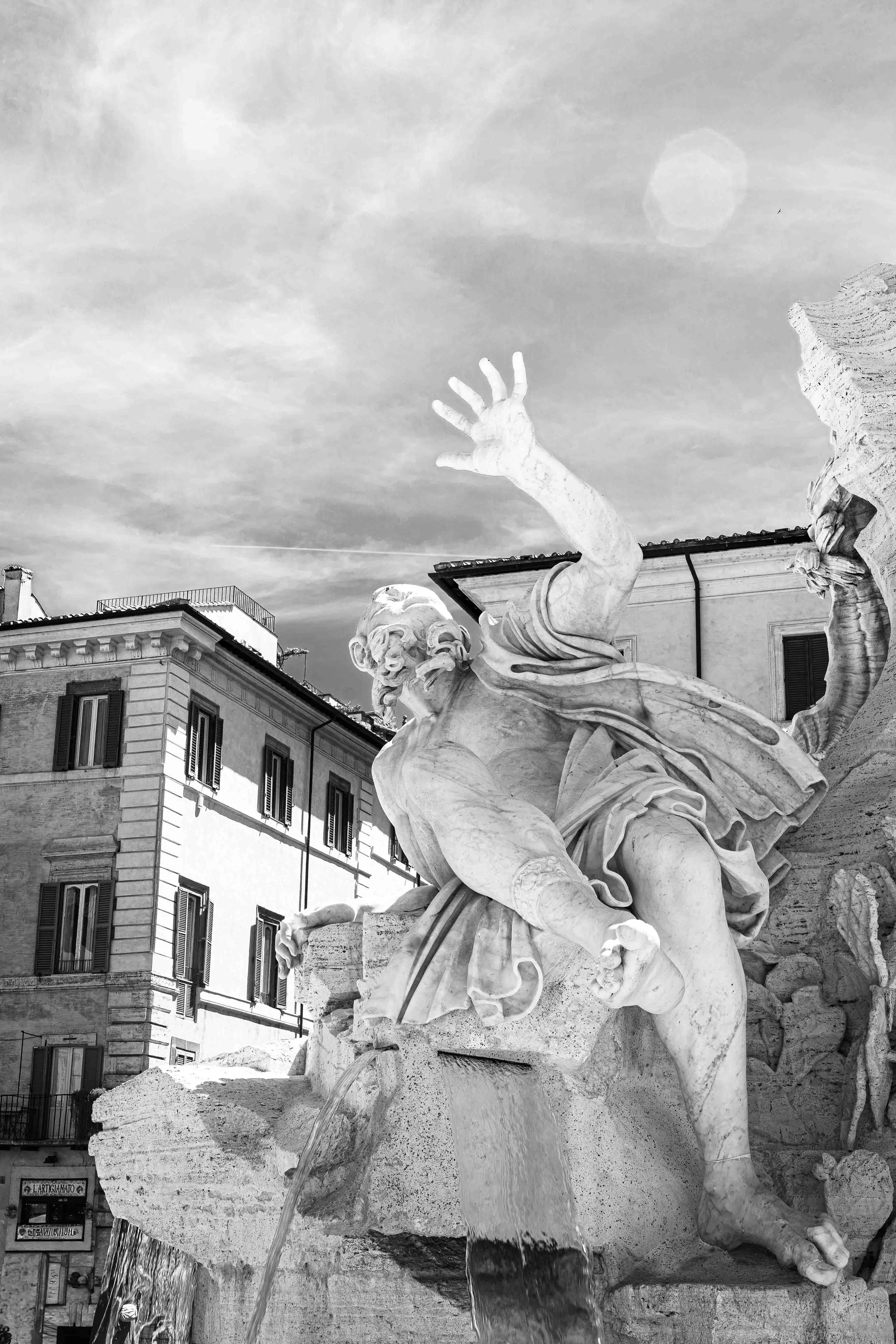 Black-and-white photograph of a dramatic marble fountain sculpture with one hand raised against the sky in Rome, Italy.