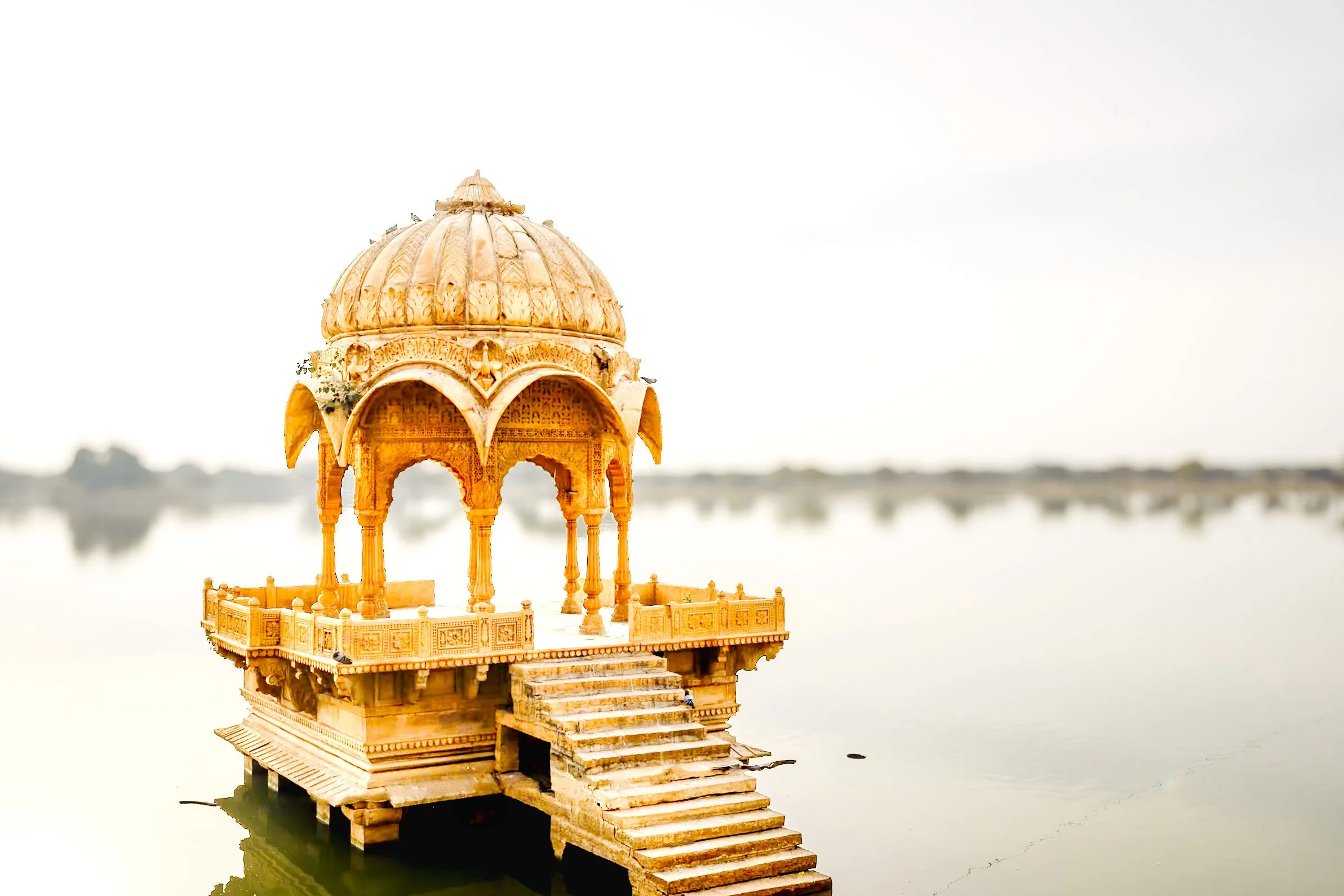 Ornate sandstone pavilion standing in still water beneath an expansive pale sky in Jaisalmer, India