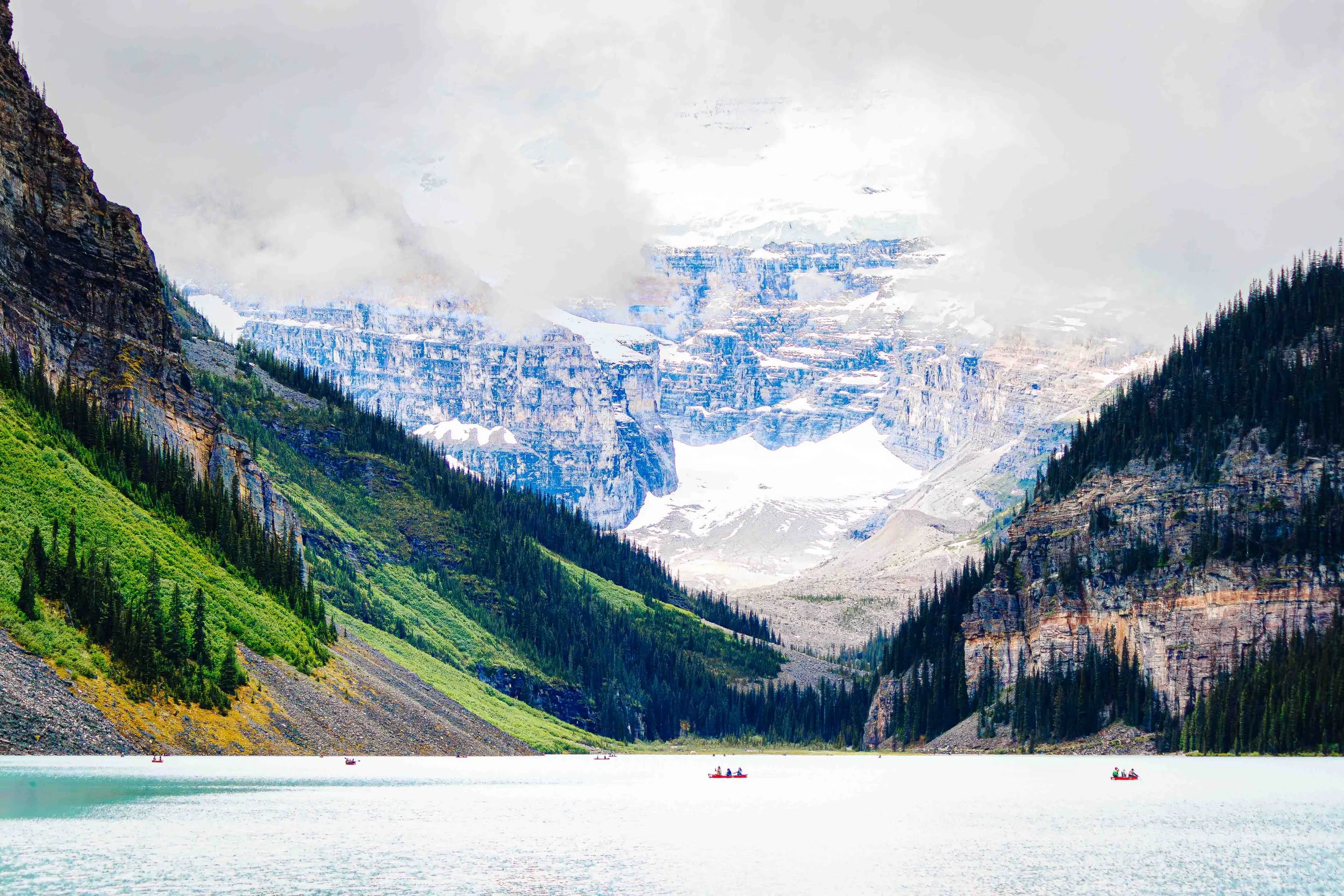 Mountain landscape rising through cloud above Lake Louise with tiny canoes on the water in Banff, Canada.