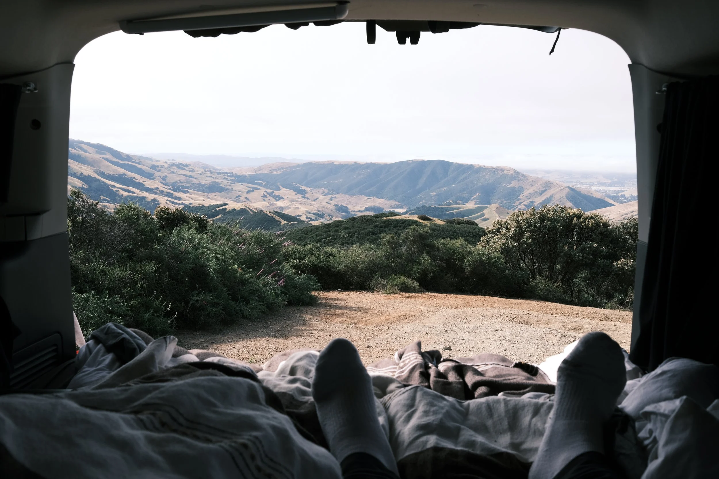 View of rolling hills and landscape from inside a car or van with a person’s sock-covered feet resting on a blanket.