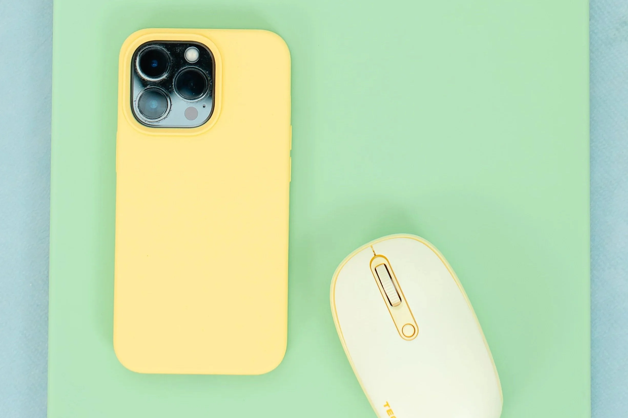 A yellow smartphone placed on a pastel green surface, next to a white wireless computer mouse.