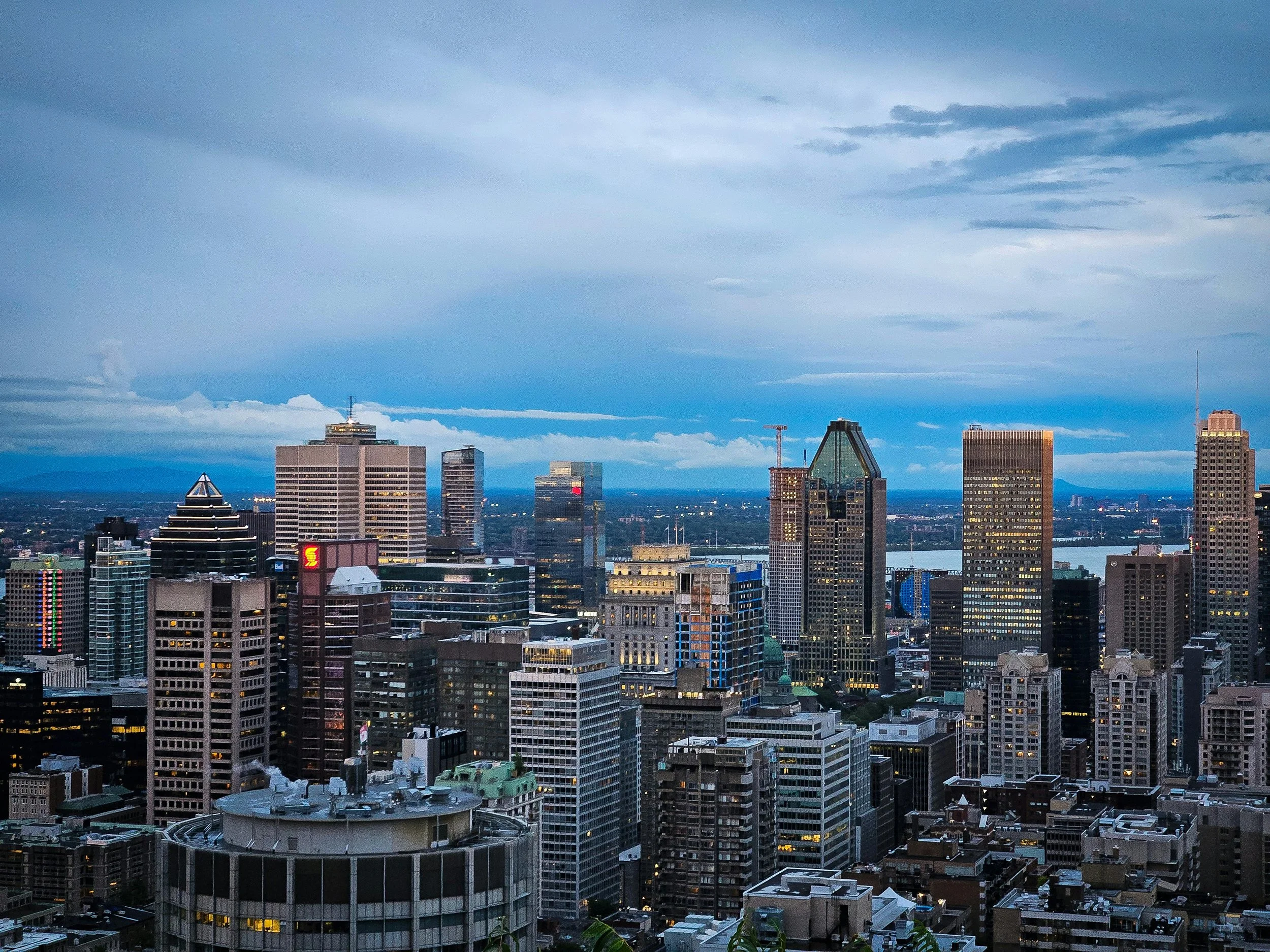 A city skyline with various tall buildings under a partly cloudy sky during dusk or early evening.