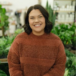 Person smiling indoors with plants in the background.