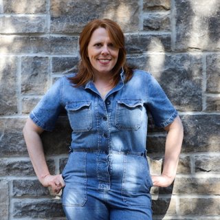 Person in a denim outfit standing against a stone wall.