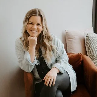 Woman sitting on a brown couch with pillows, smiling