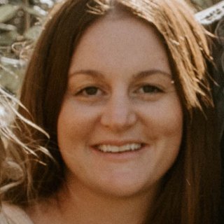 A person with long brown hair smiling outdoors.