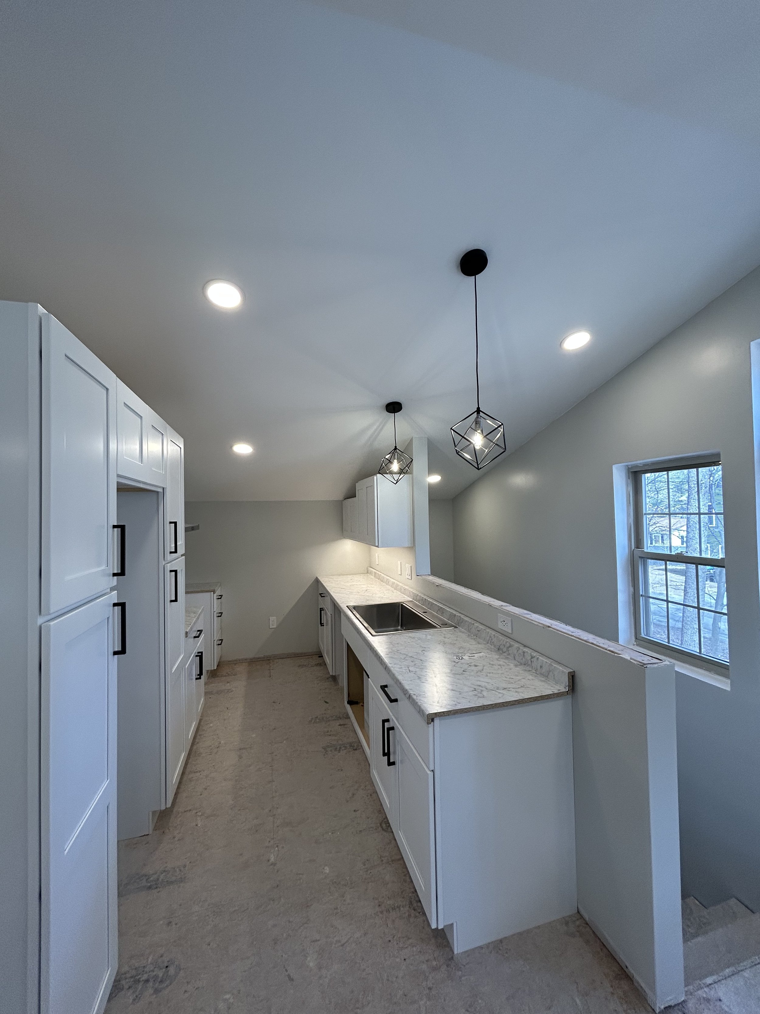 Modern kitchen with white cabinets, marble countertops, pendant lights, and a large window.