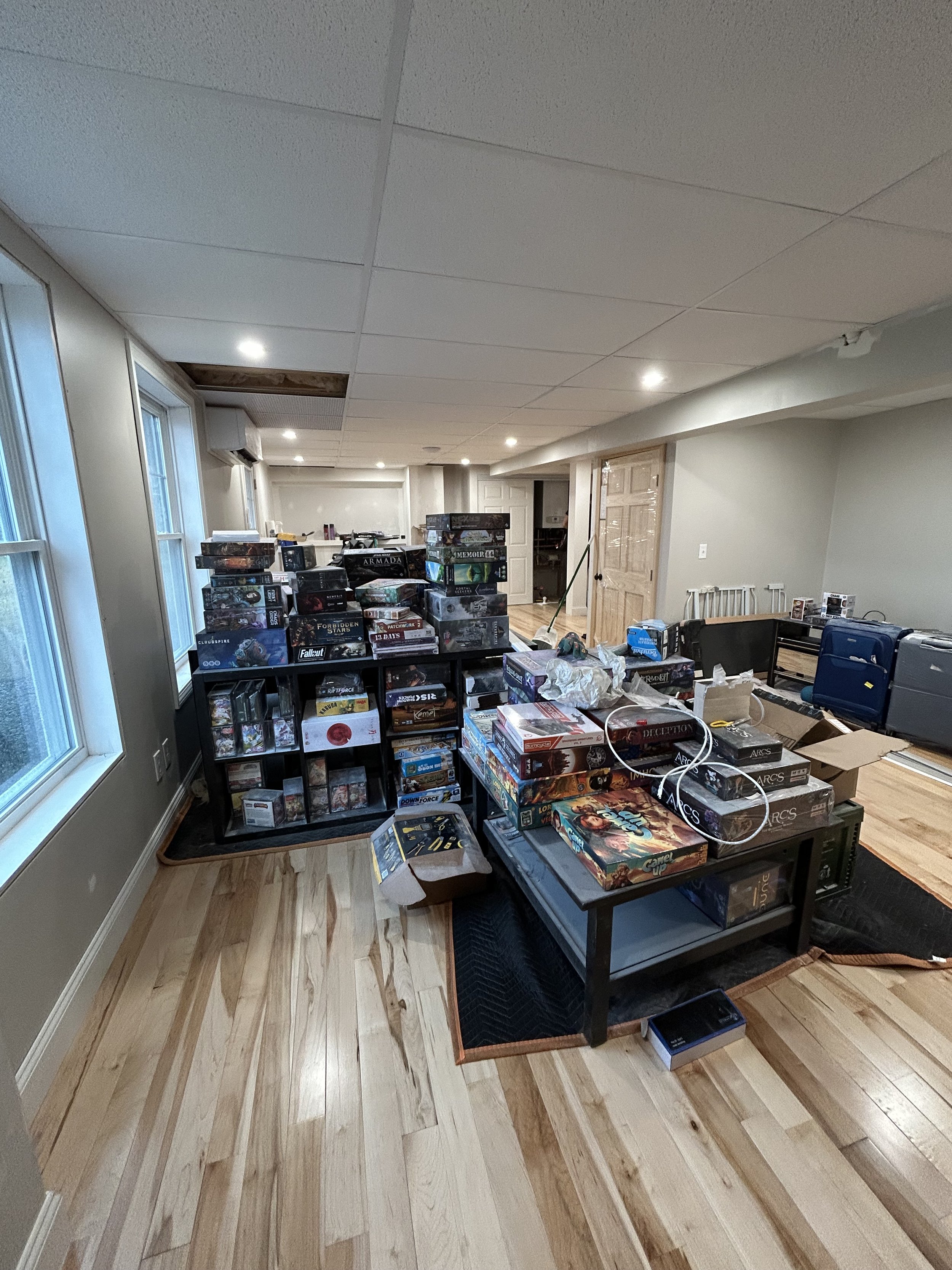A room with wood flooring filled with stacked board games on shelves and tables, including various popular titles.