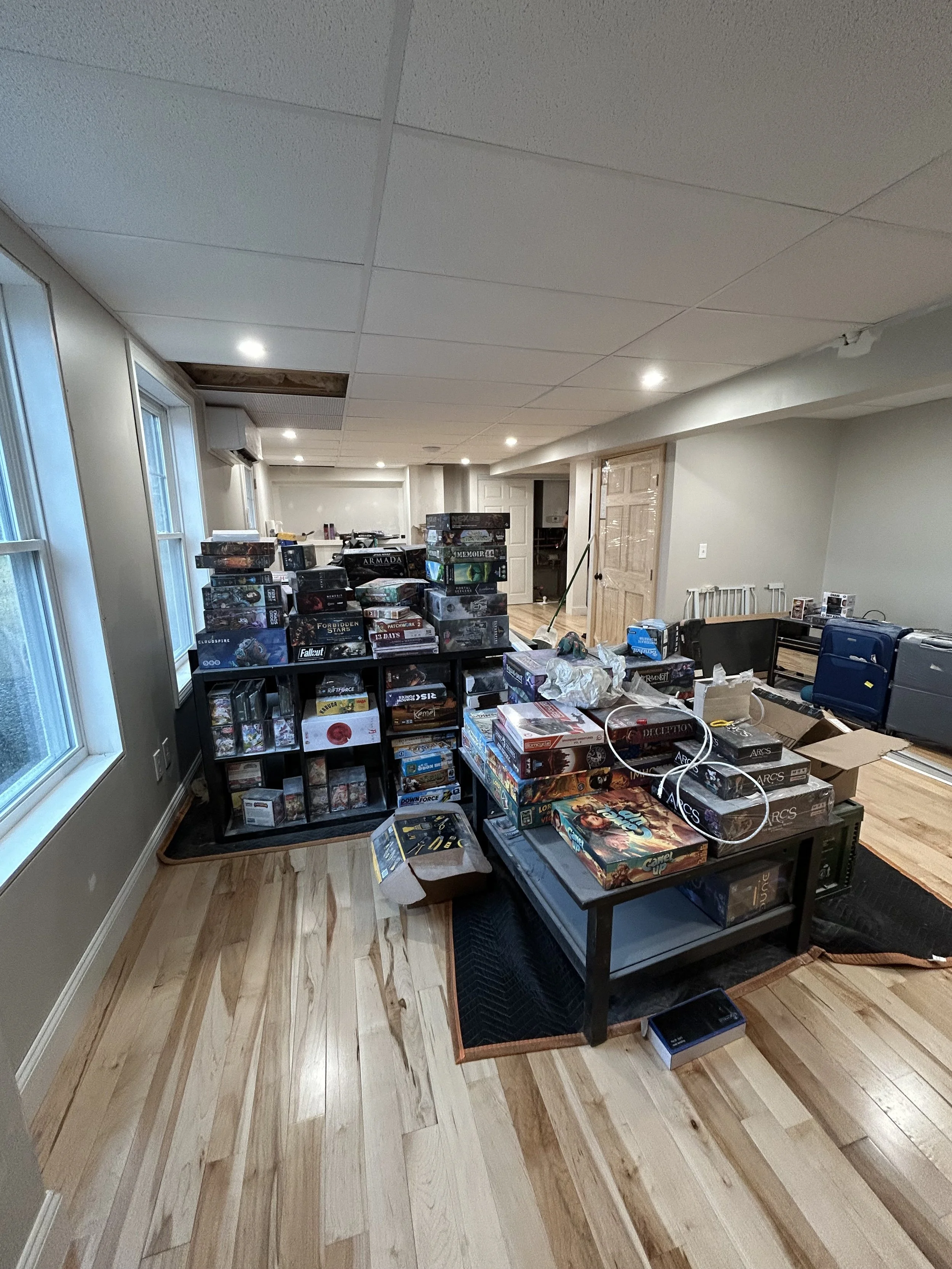 A room with wood flooring filled with stacked board games on shelves and tables, including various popular titles.