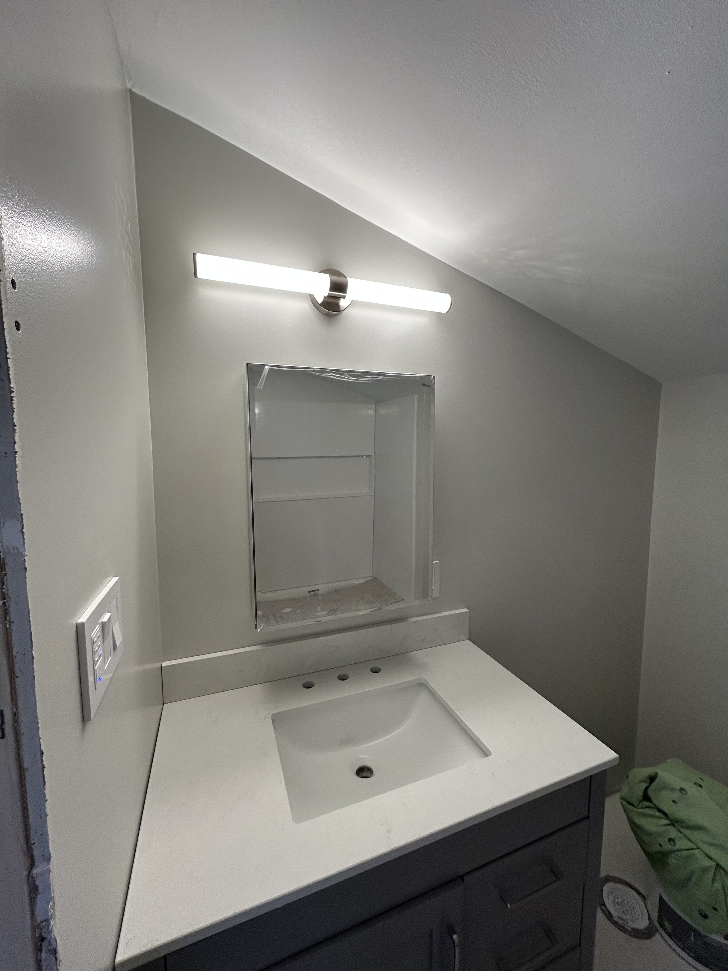 Bathroom sink with white countertop, wall-mounted vanity light, and mirror space