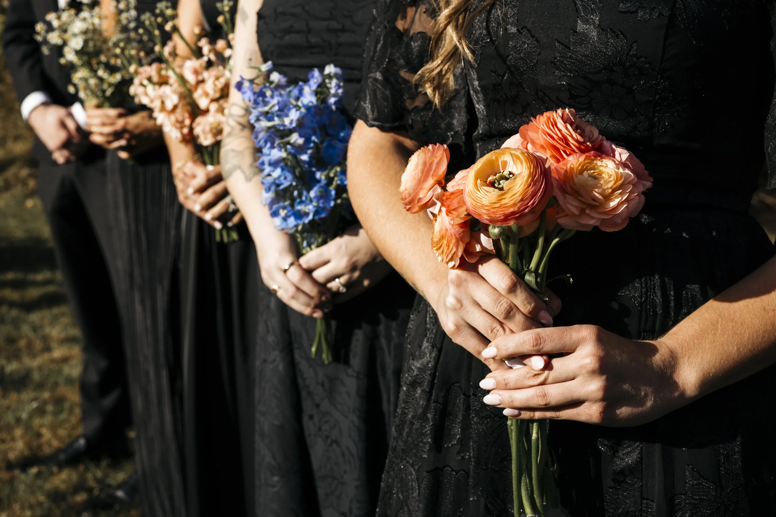 Group of people dressed in formal attire holding colorful bouquets of flowers, standing outdoors.