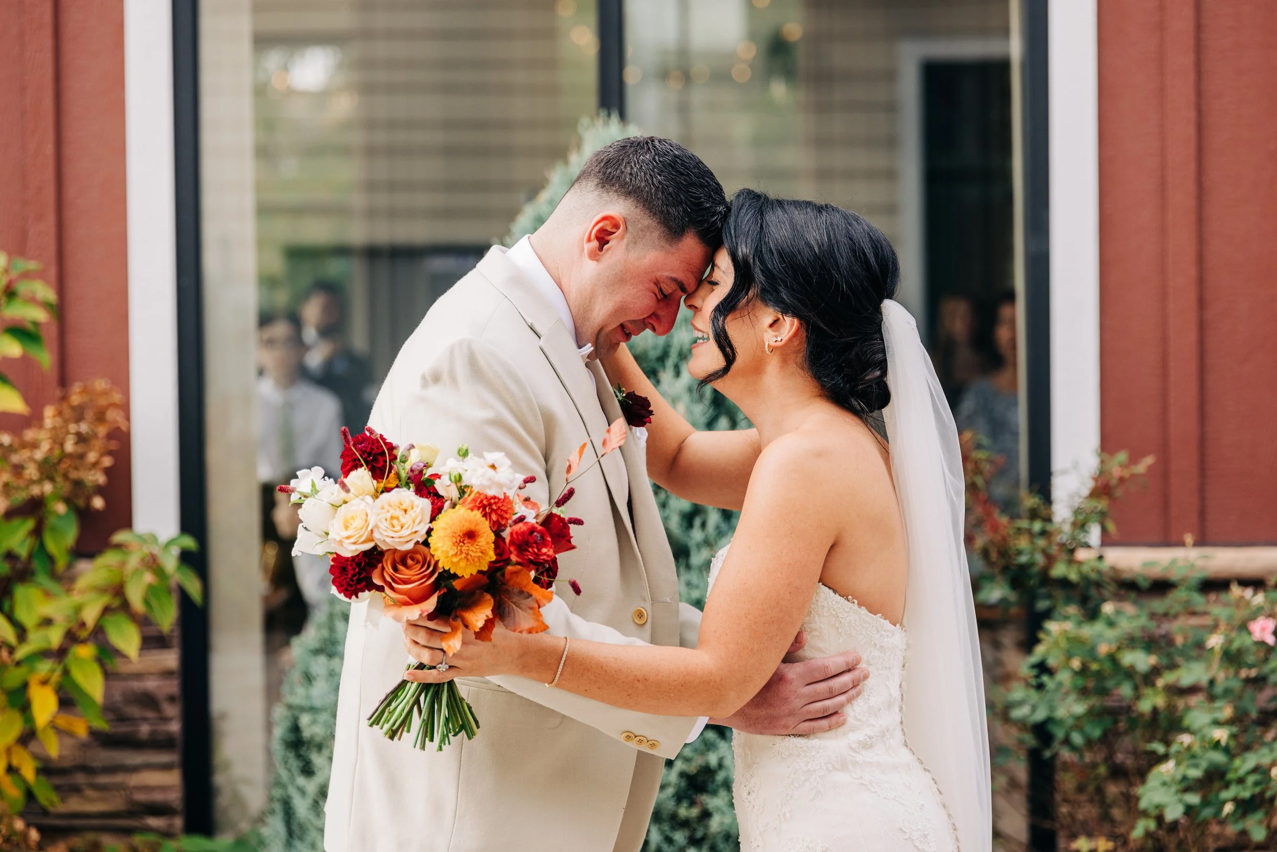 A bride and groom share a joyful moment, touching foreheads and smiling, with the bride holding a colorful bouquet of flowers.