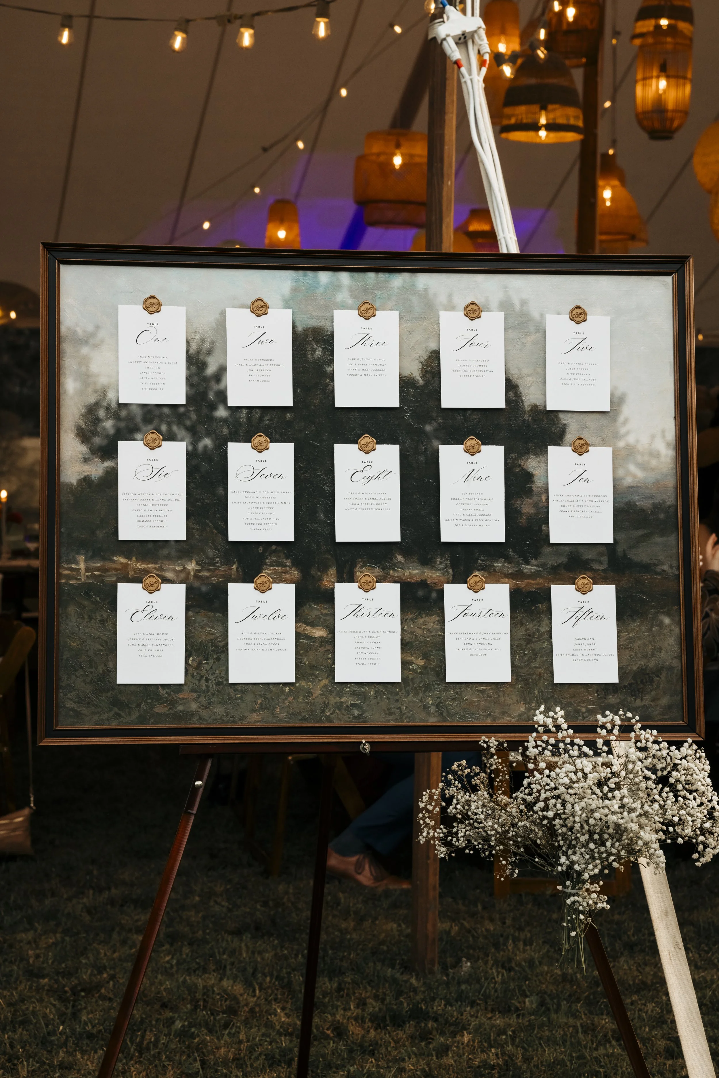 Wedding seating chart board with numbered table cards, flowers, and string lights overhead.