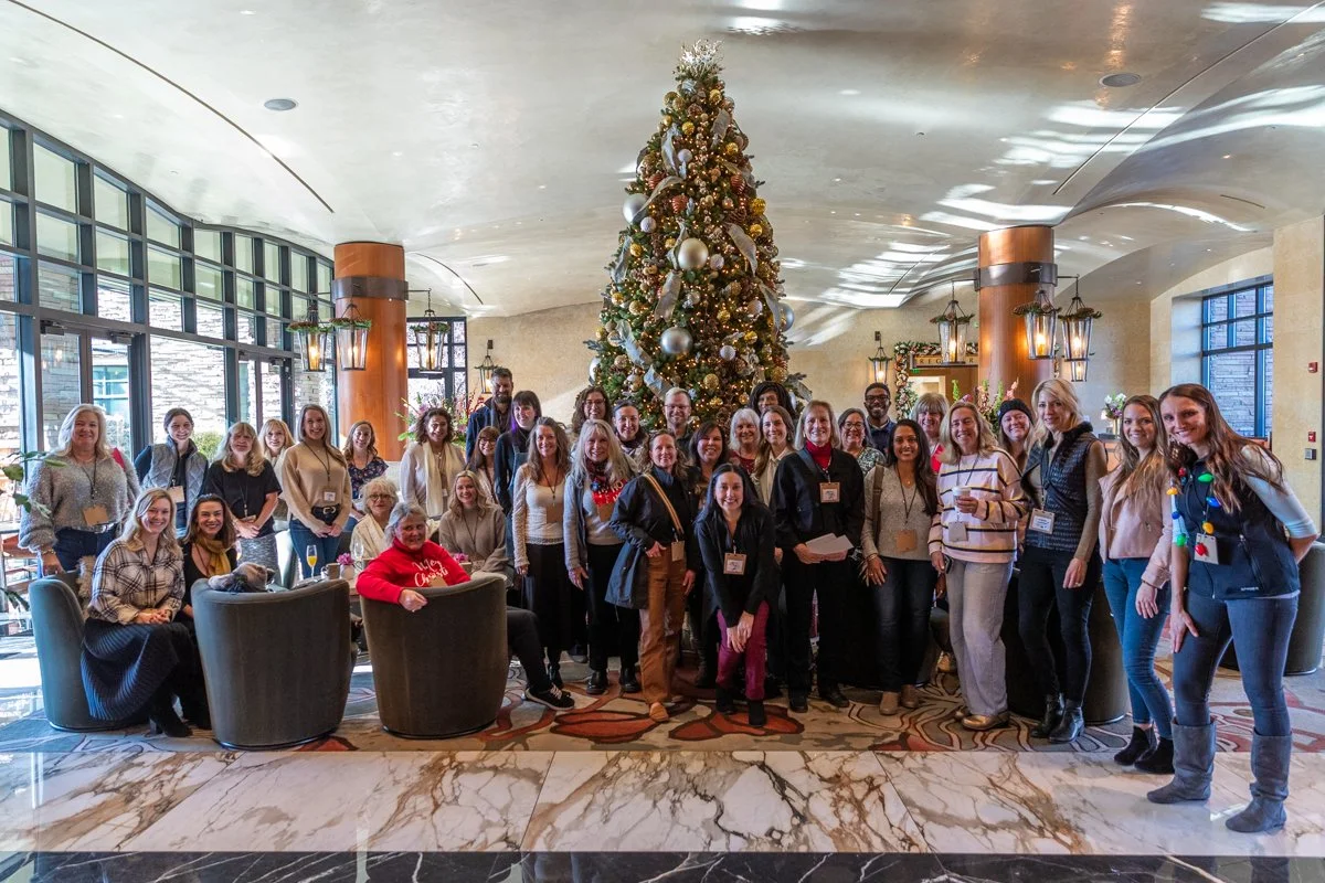 Group photo of a large group of professionals in front of a large Christmas tree in a high end hotel lounge.