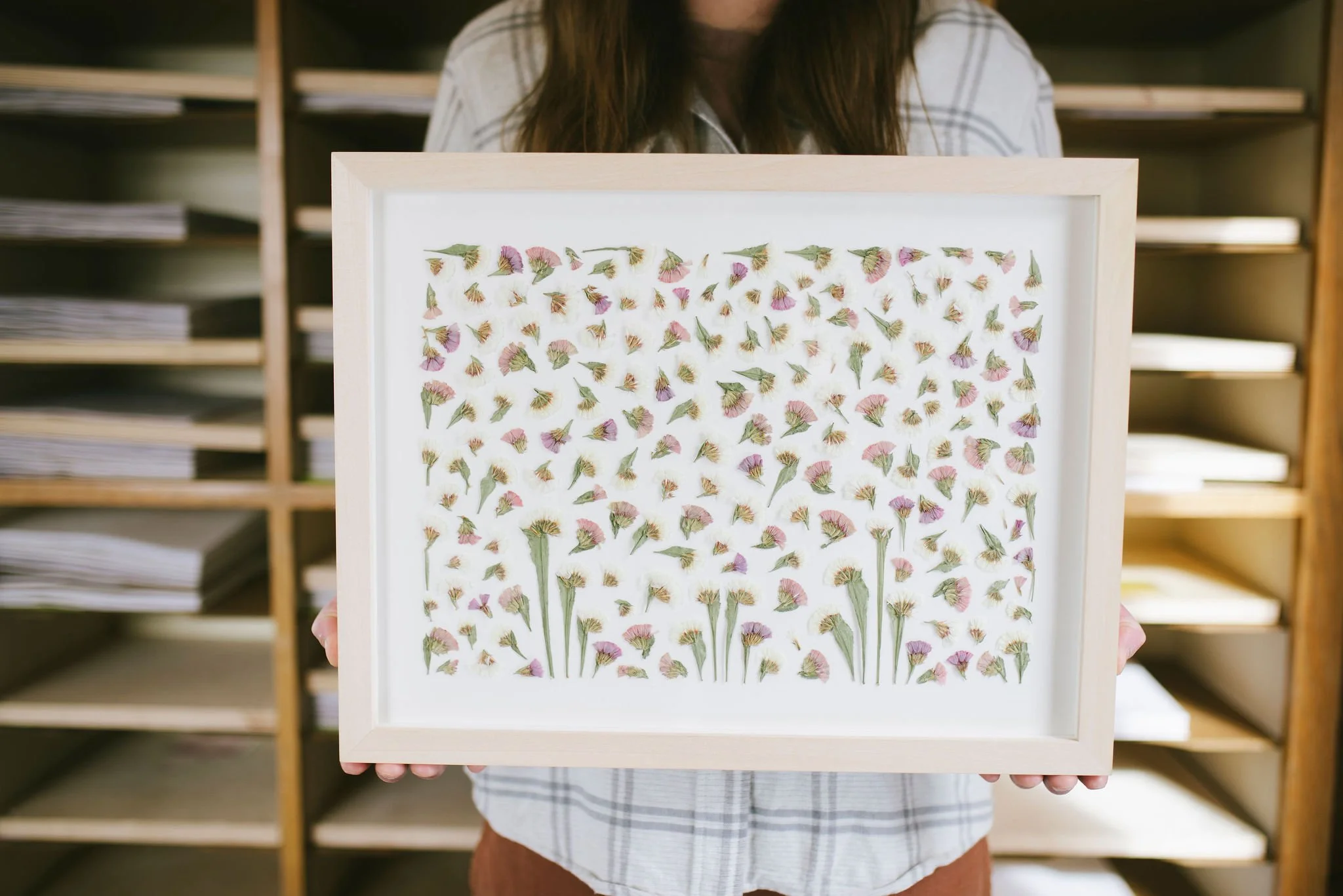 Framed pressed pink and white status. The artist is holding the framed piece inside of her studio. 