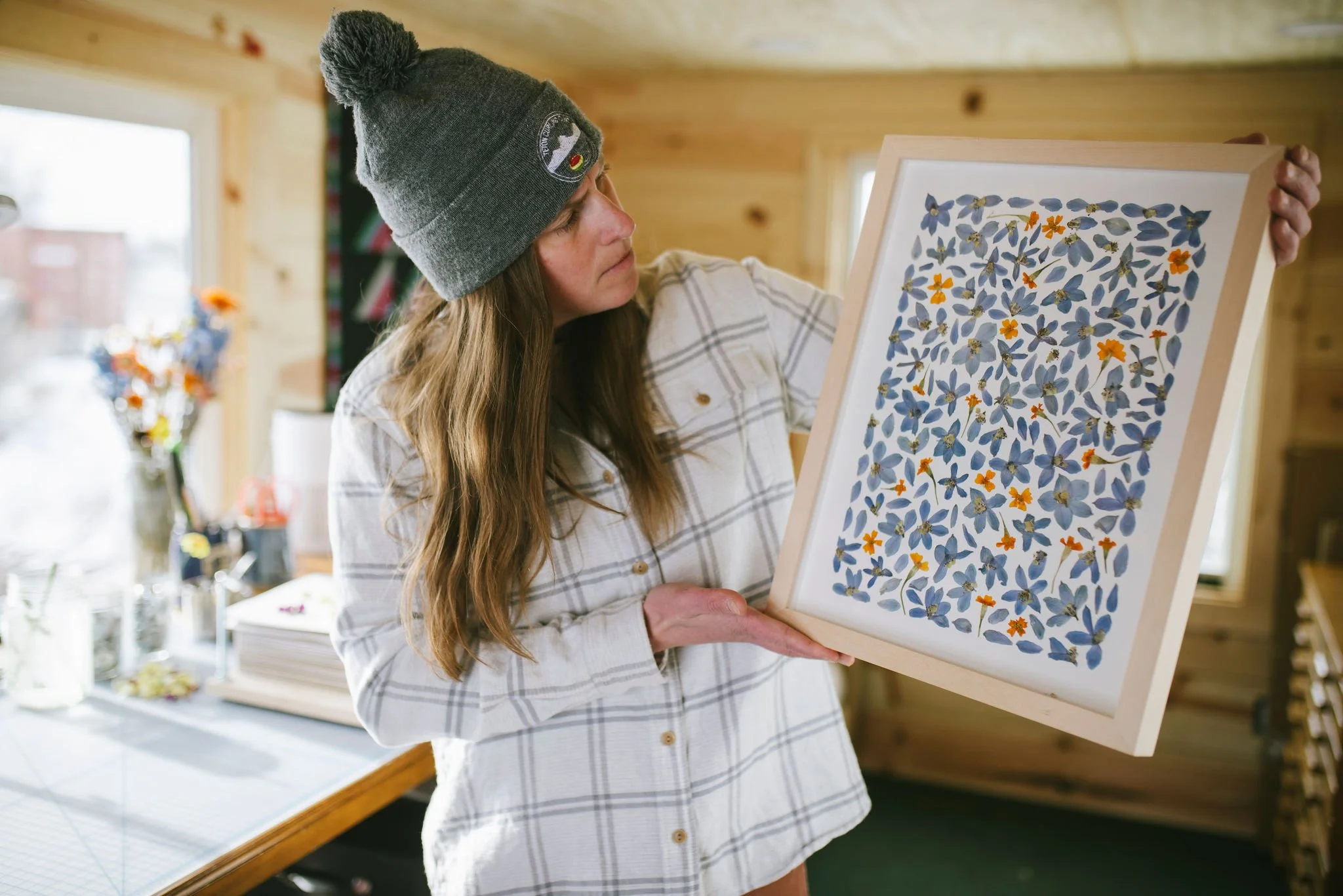 A framed original piece of pressed flower artwork including delphinium and tiny marigold flowers. 