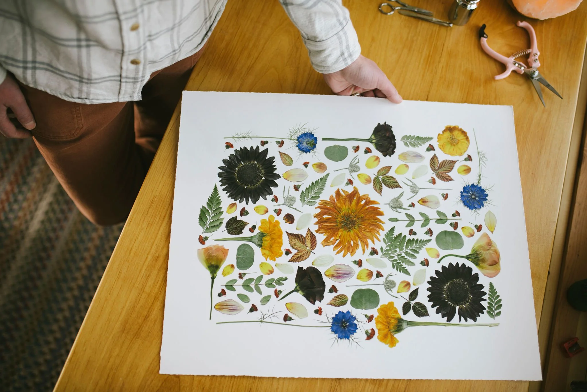 An image of the artist holding a fine art print of an original pressed flower piece from a Teton Valley wedding.