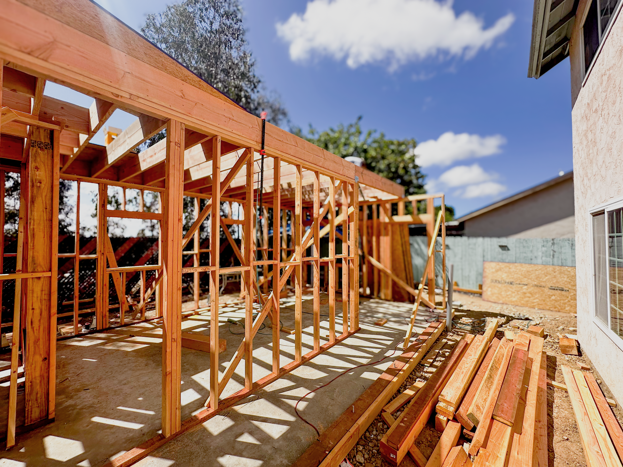 Wooden framing for house construction in progress on a sunny day with blue sky and white clouds.