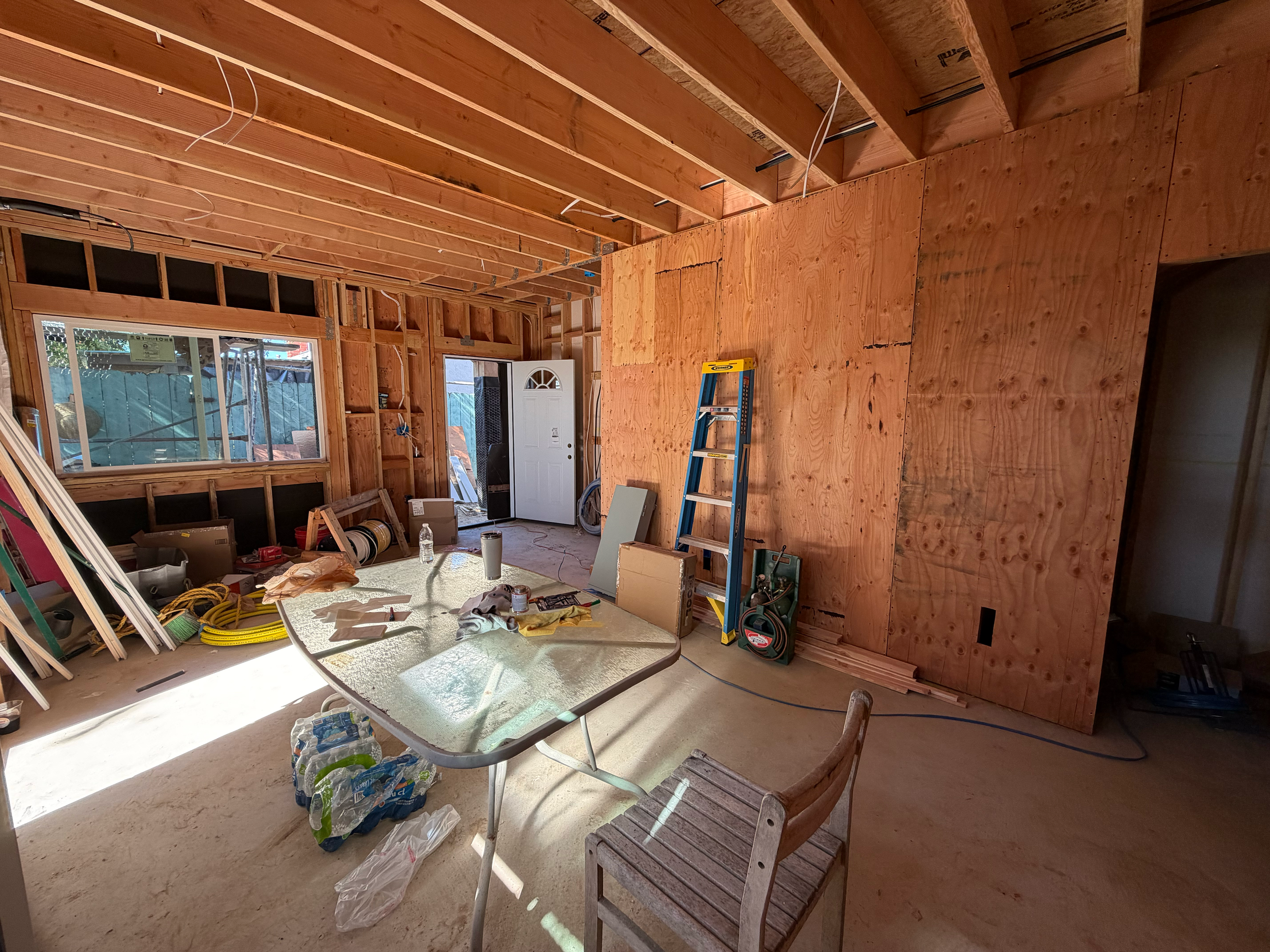 Interior of a house under construction with exposed wooden framing, a table with construction tools, and a ladder.