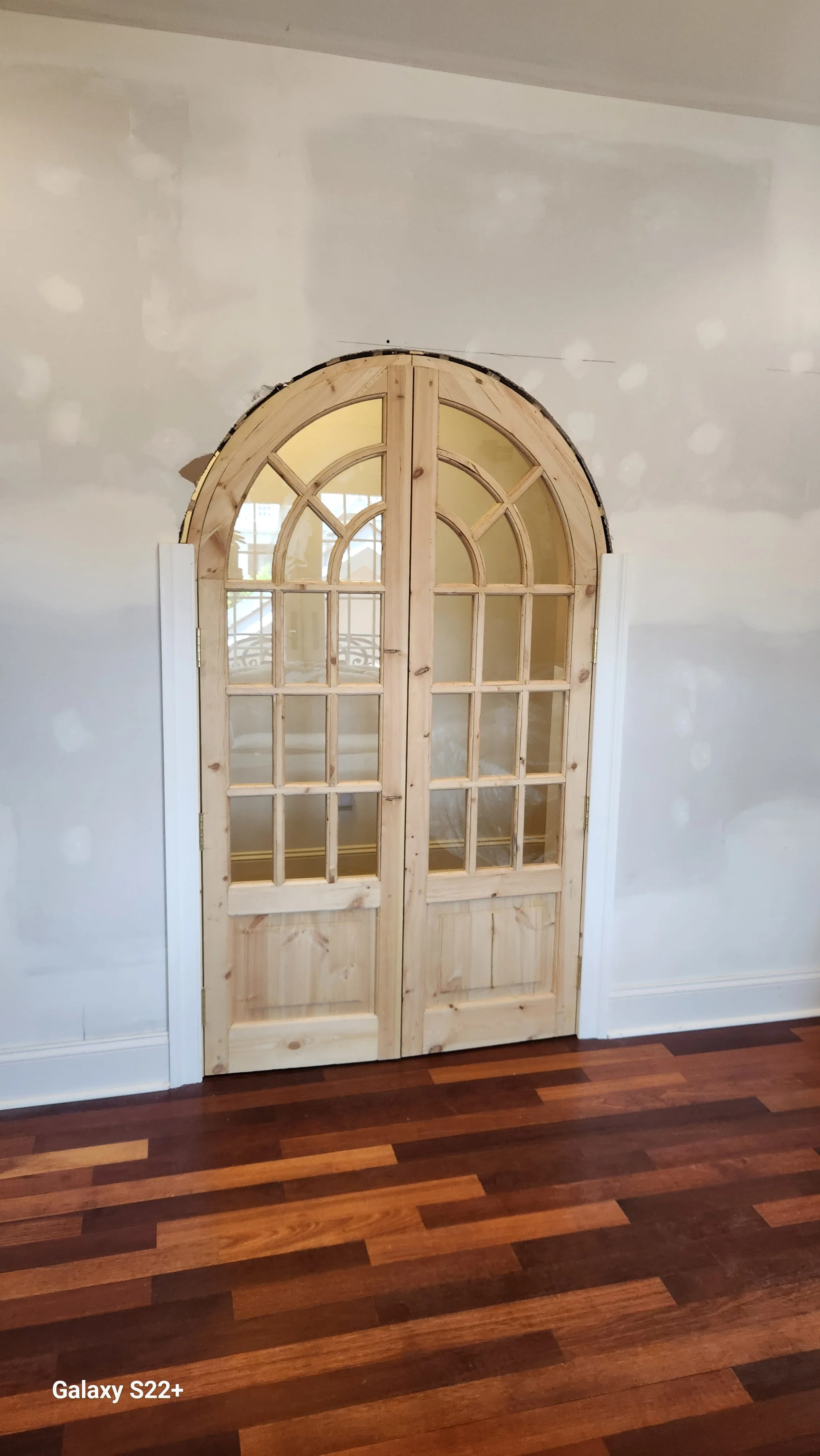 Unfinished interior wall with a set of double wooden French doors and a hardwood floor.