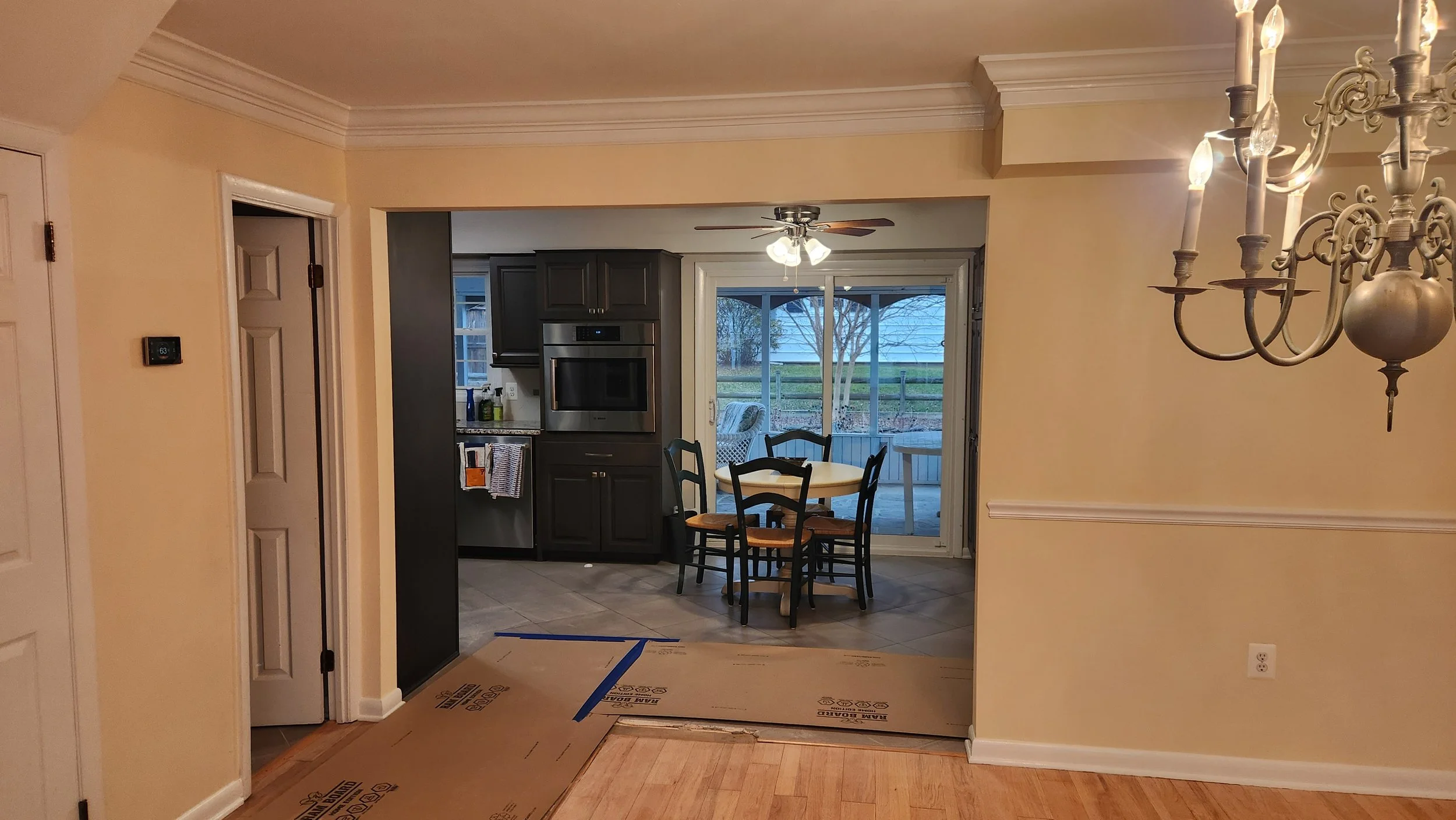 View of a kitchen and dining area in a home interior, with a sliding glass door leading to an outdoor patio, a round dining table with four chairs, dark cabinetry, a ceiling fan, and a chandelier.