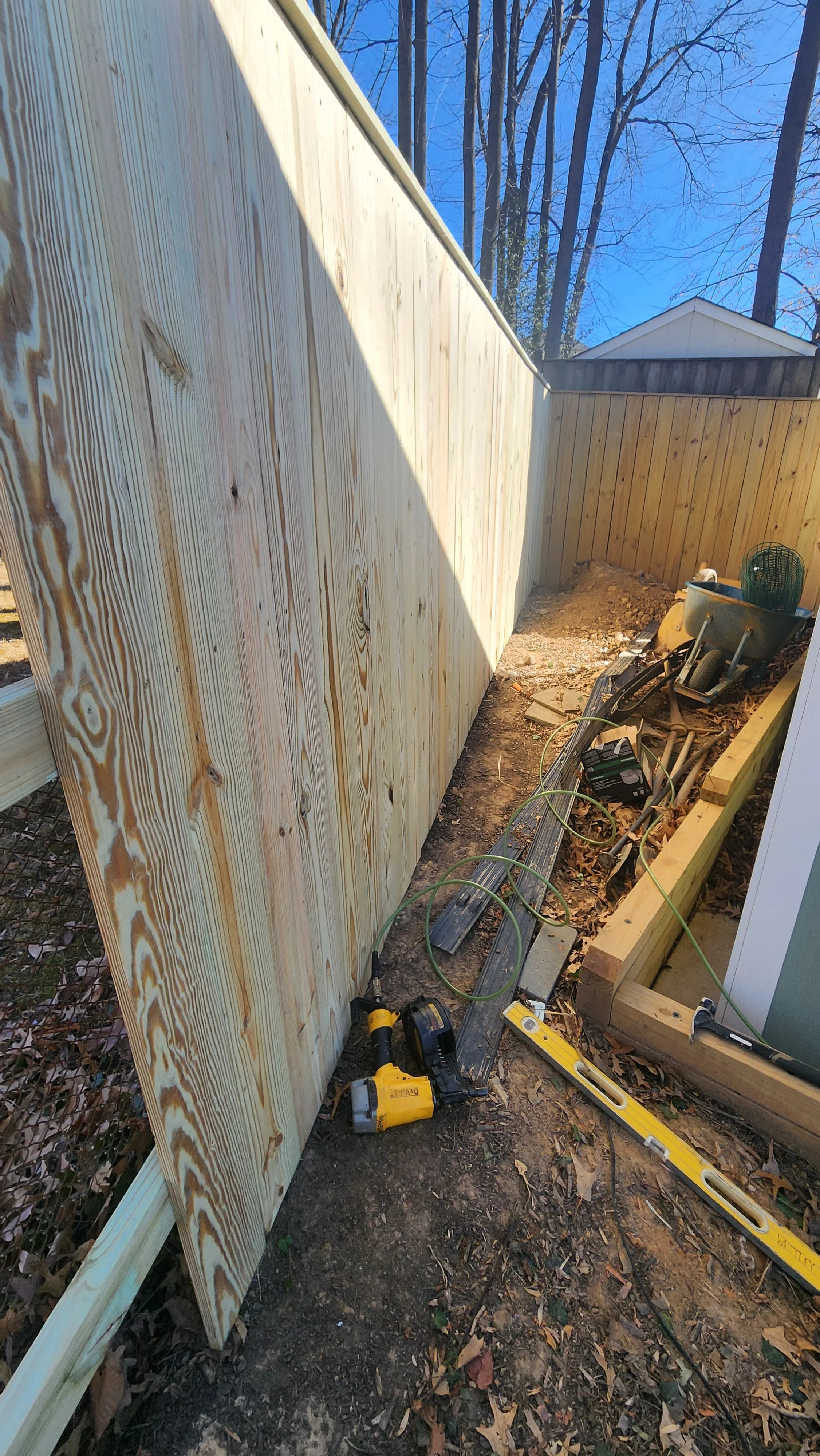 Construction site with wooden fence panels, tools, and construction materials in a backyard.