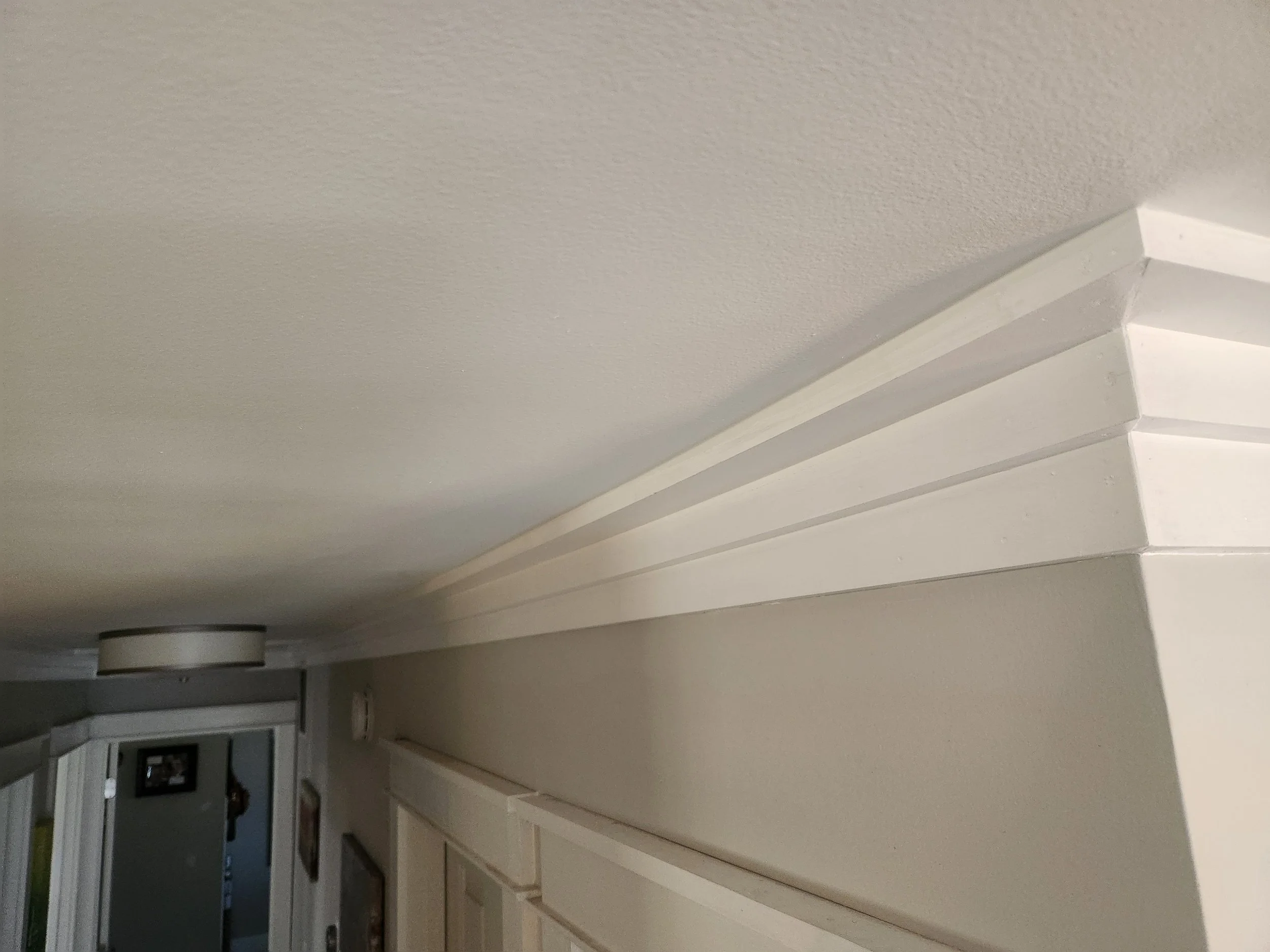 Close-up of a white crown molding on a ceiling, with part of the door frame and doorway visible in the background.