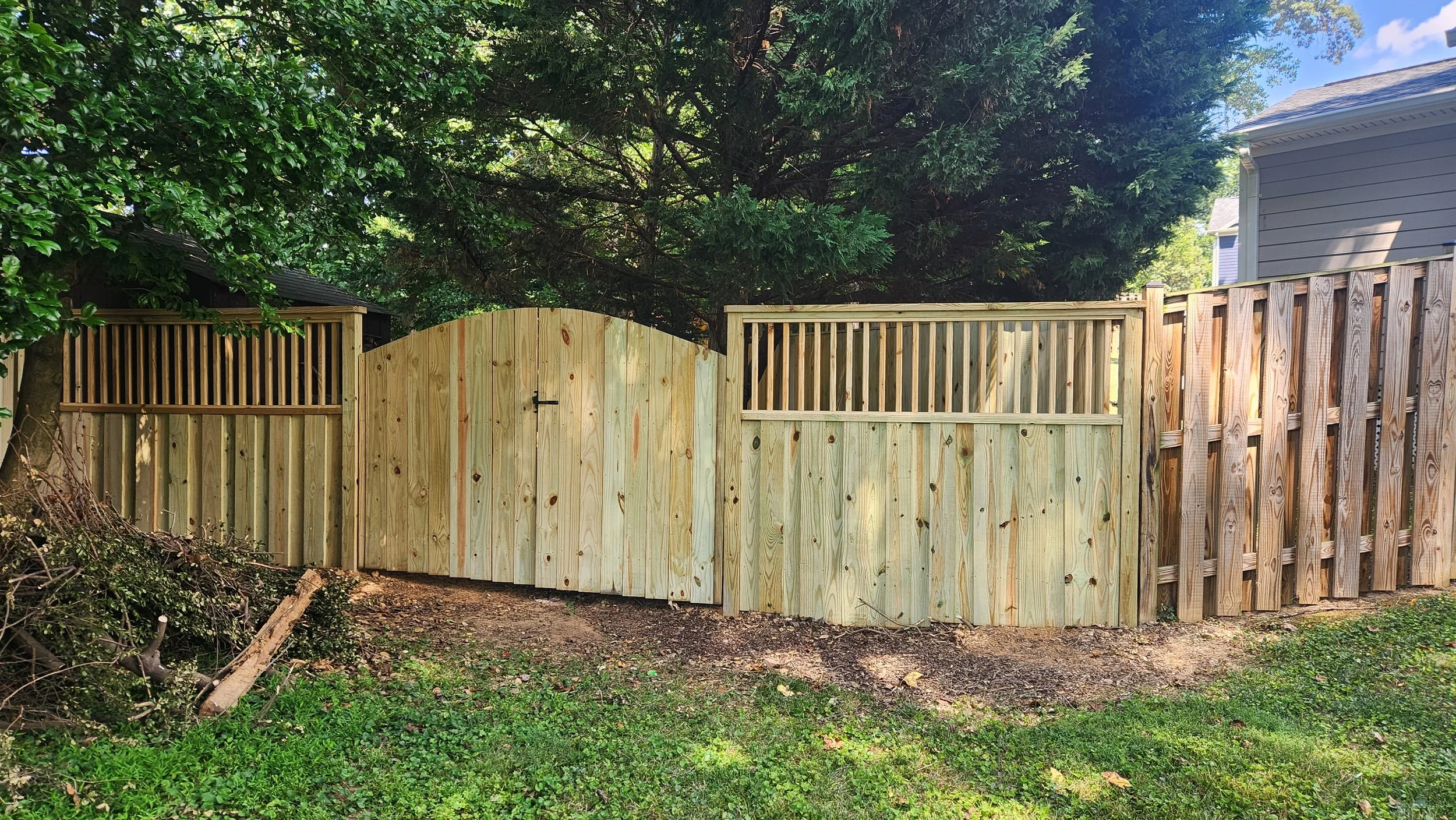 Wooden backyard fence with gate, surrounded by green trees and grass.