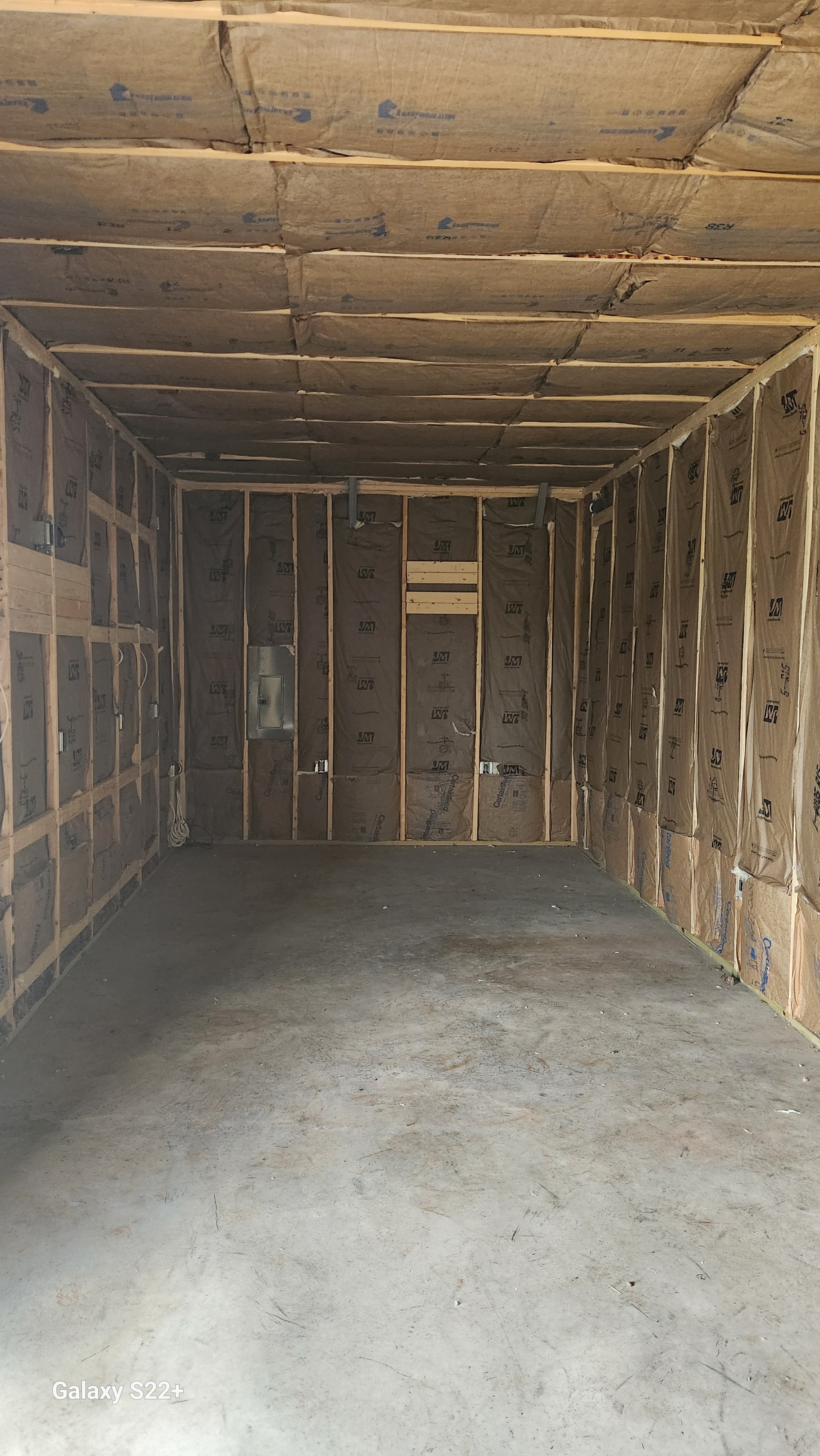 Empty garage with insulation installed on the walls and ceiling, exposed wooden framing, and a concrete floor.