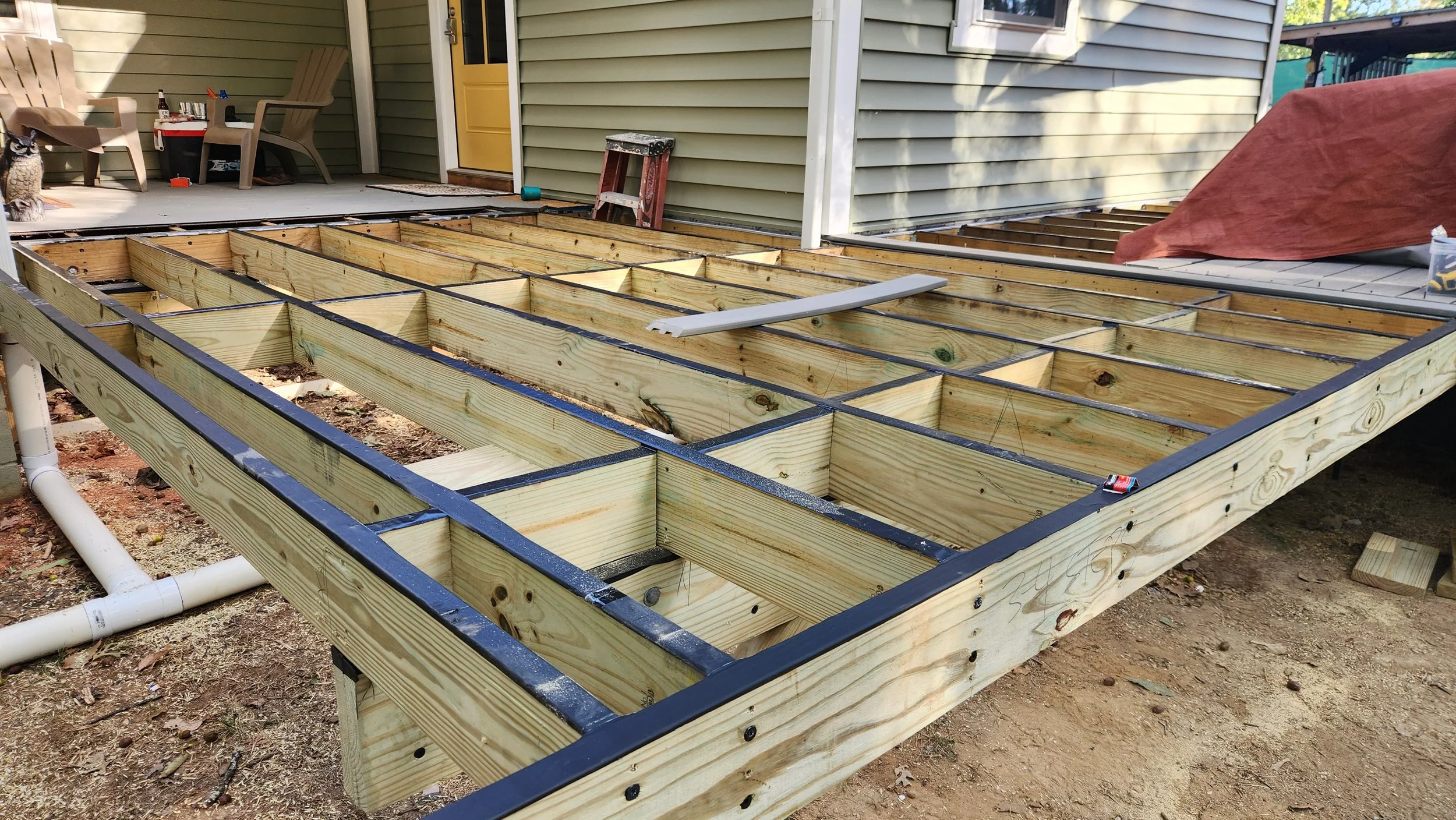Wooden deck framing under construction in a backyard, with some tools and materials visible around.