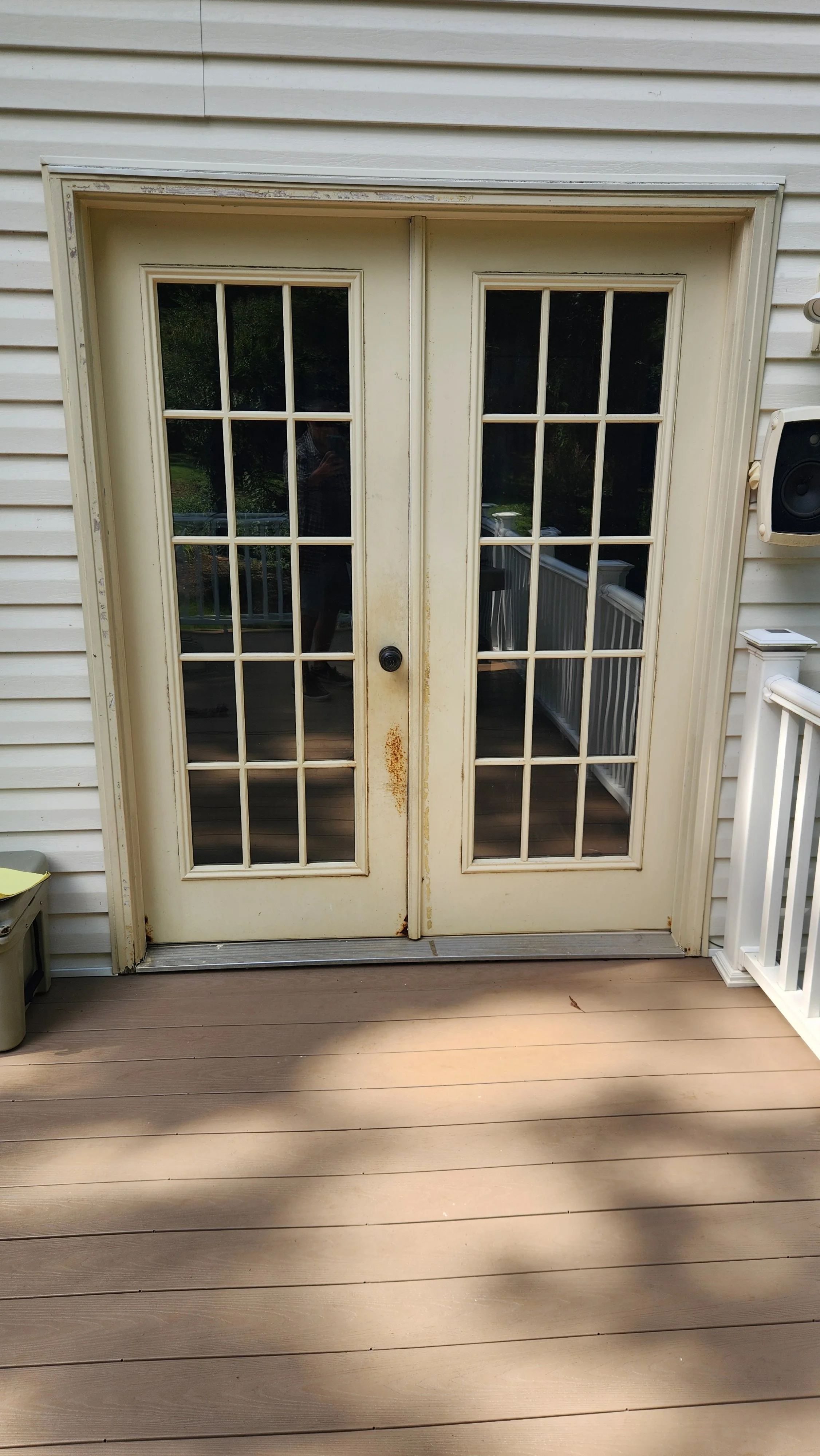 A set of double glass patio doors with white frames, some rust stains on the middle handles, leading to an outdoor wooden deck.