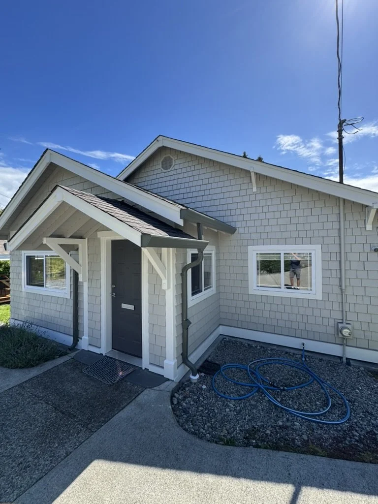 A beige house with white trim and a small front porch under a bright blue sky with a few clouds.