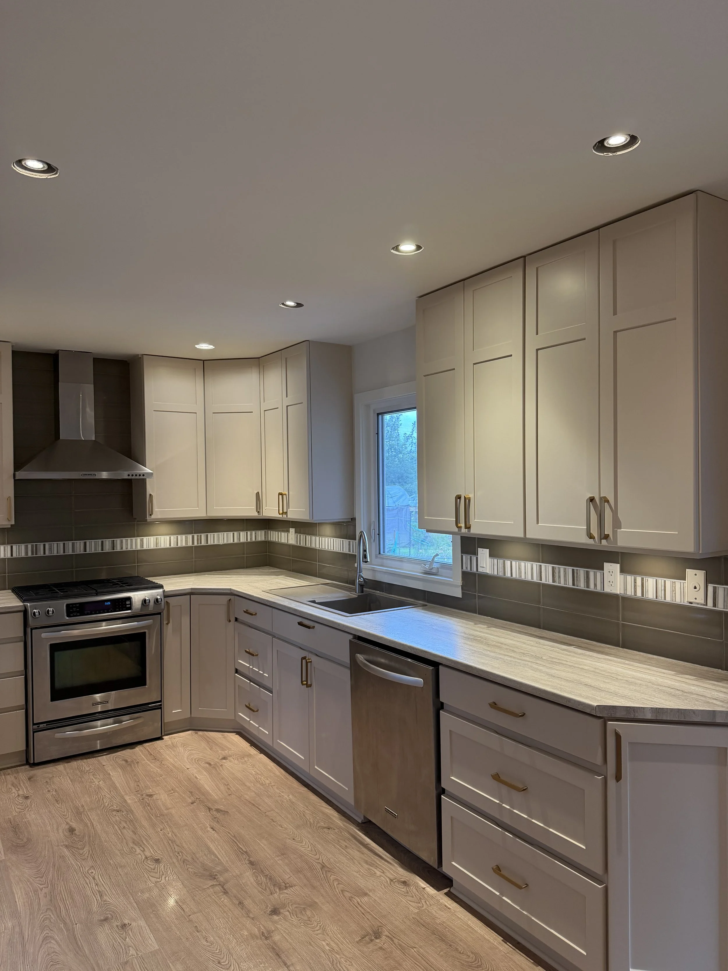 Modern kitchen with cream-colored cabinets, stainless steel appliances, a window above the sink, and wood flooring.