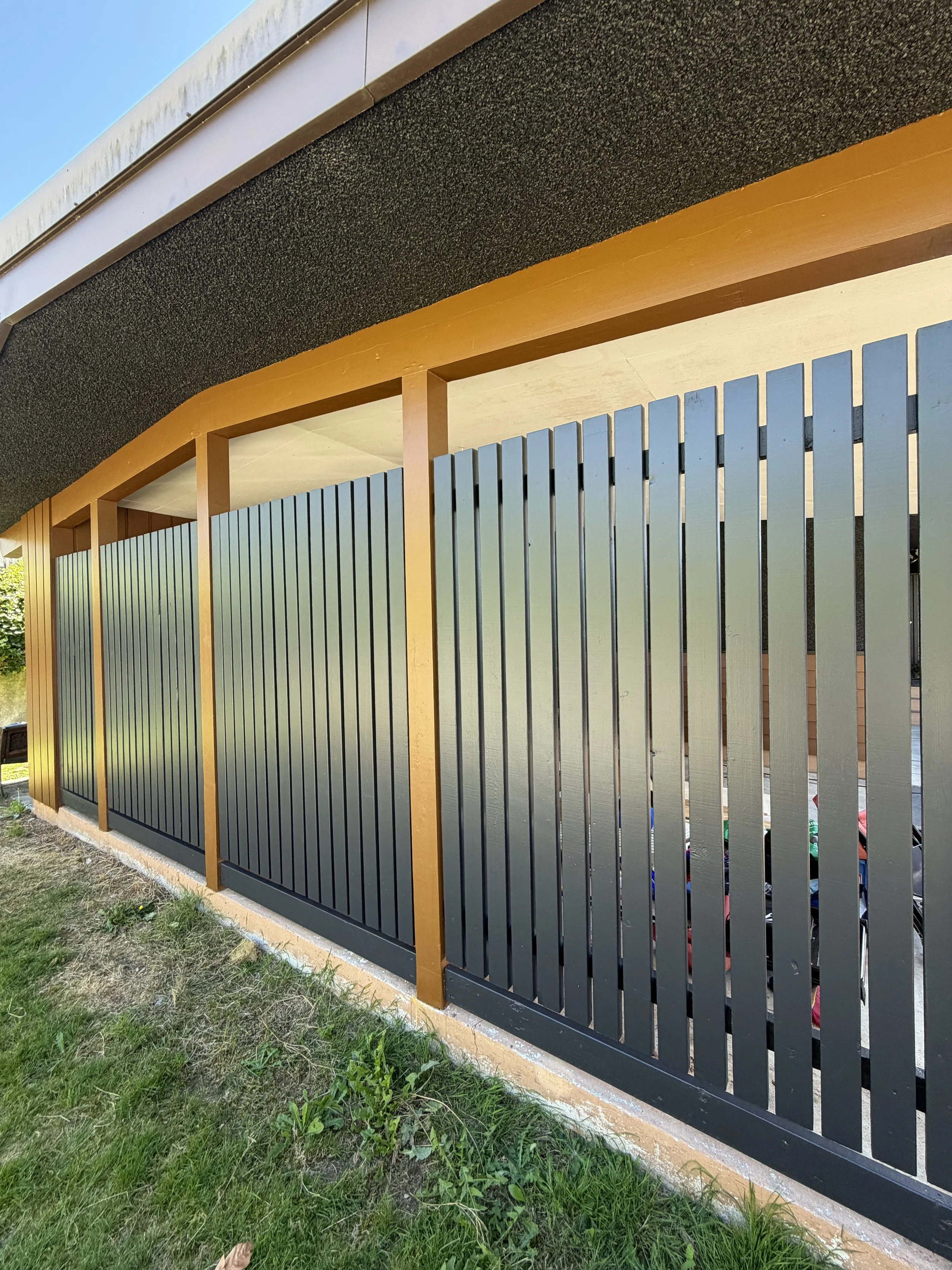 A modern black metal fence with vertical slats and wooden posts, located next to a grassy area.