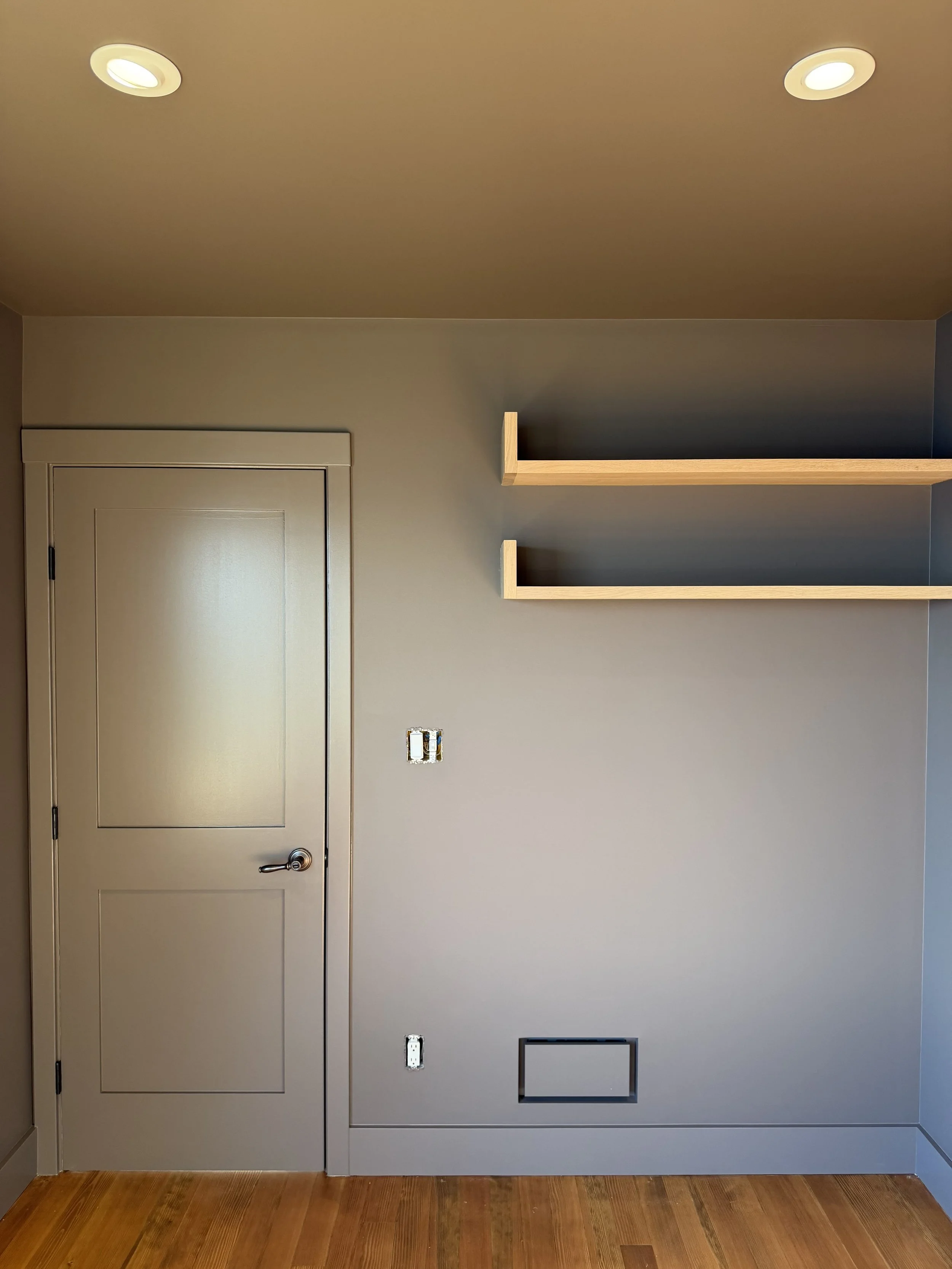 Interior wall with a closed door, two wooden shelves, electrical outlets, and a floor vent, all in a modern minimalist style.
