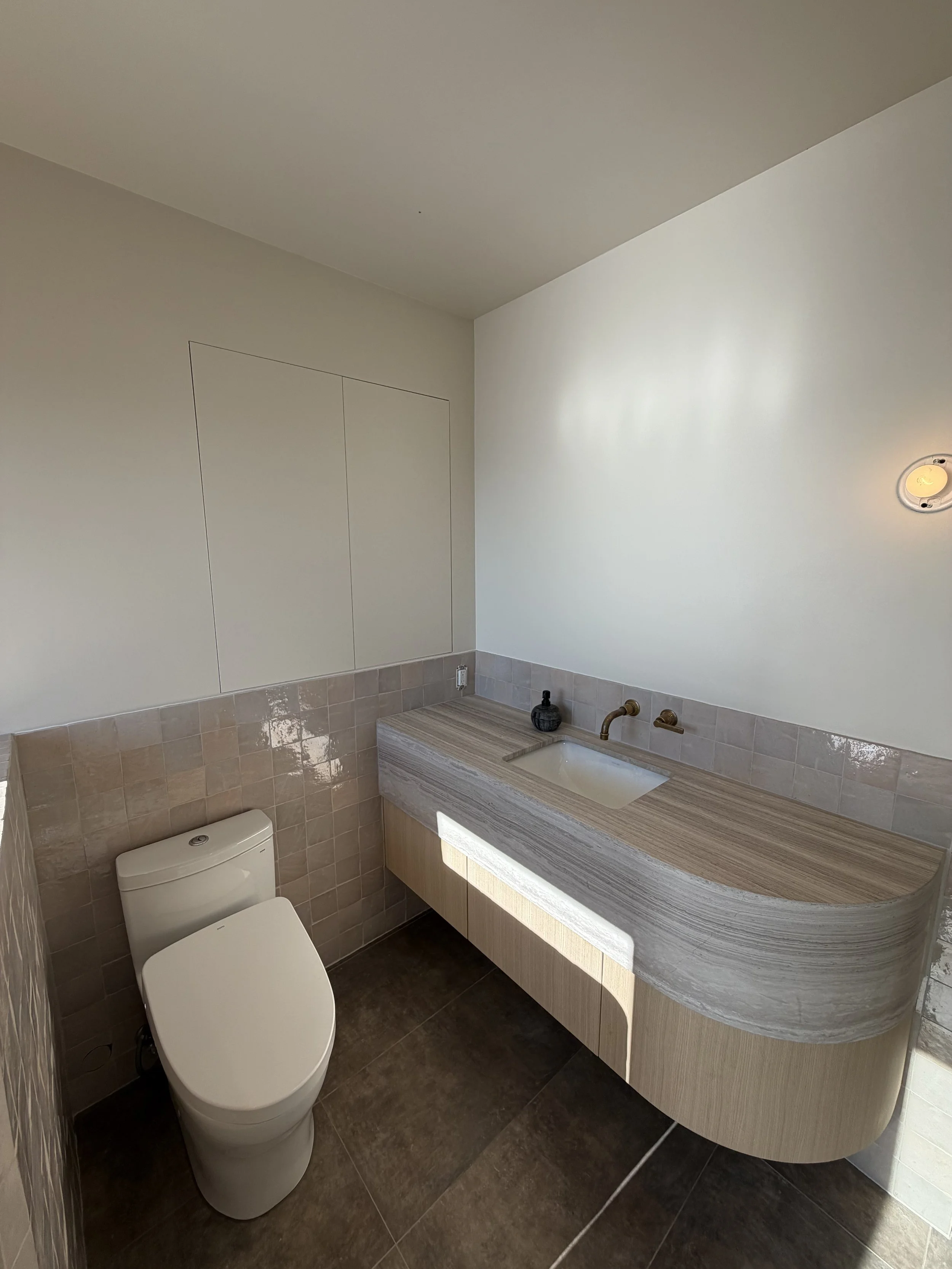 Modern bathroom with a toilet, a curved vanity with a sink, and tiled walls and floor.