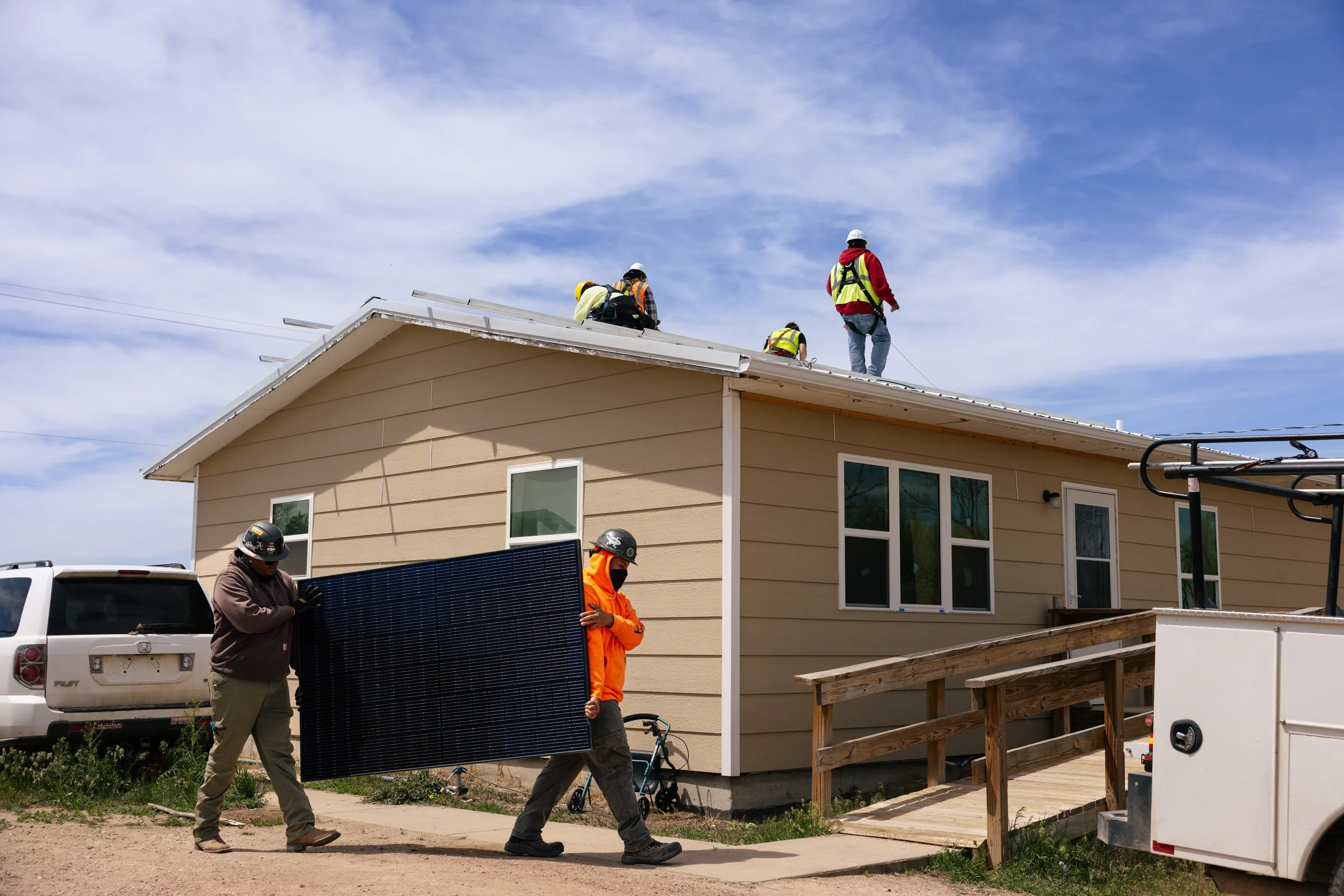 GRID Alternatives installers carry a solar panel toward a home during a residential installation at the Pine Ridge Indian Reservation, South Dakota.