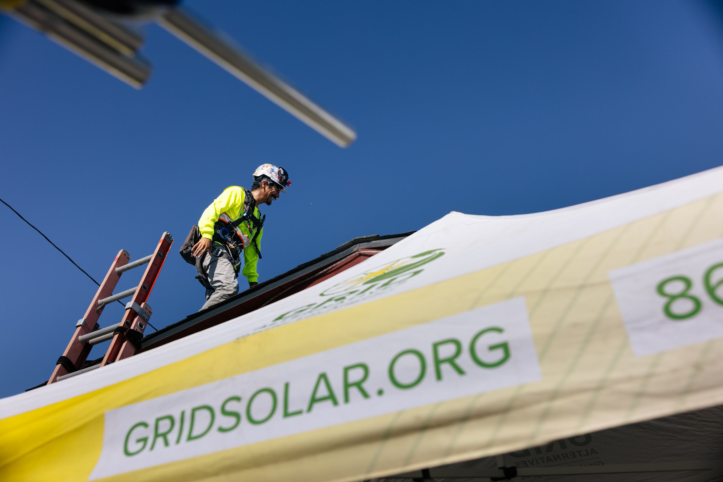 A GRID Alternatives installer works on a residential rooftop solar installation in Los Angeles, California, with the GRIDSOLAR.ORG banner visible below.