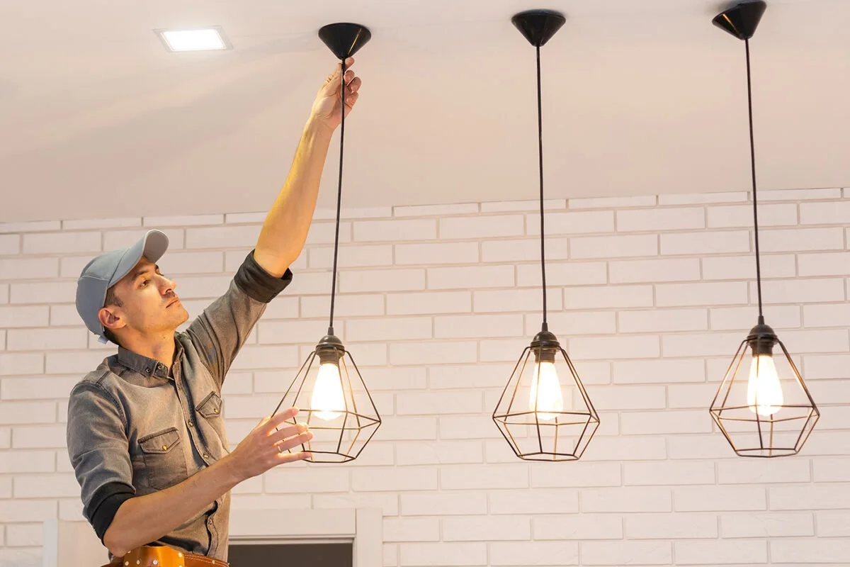 Man installing a black pendant light fixture in a modern interior with white brick walls.