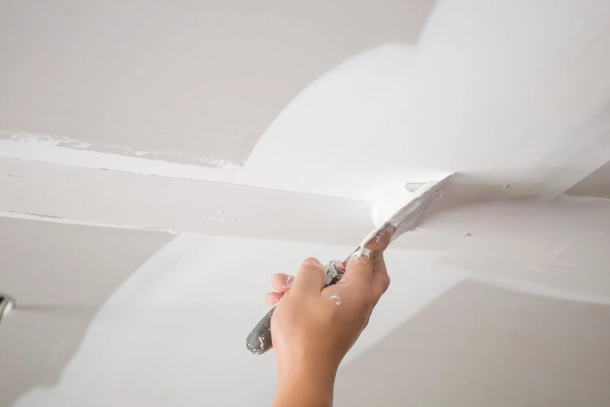 Person applying white paint to the ceiling with a paintbrush.