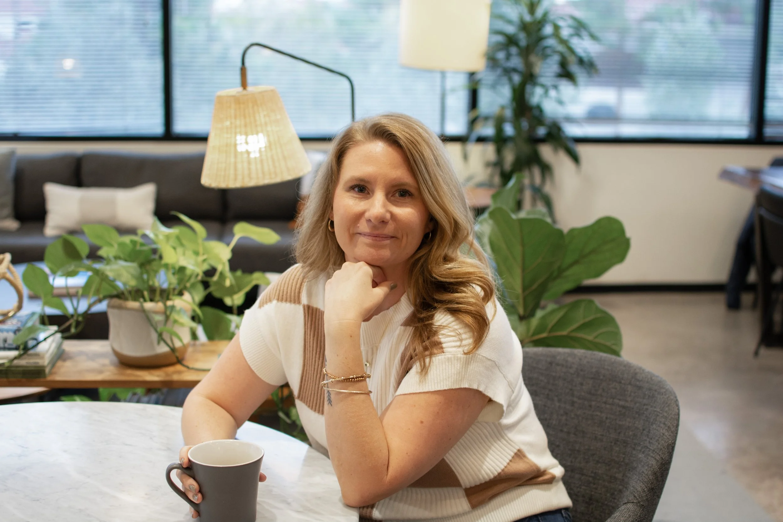 Owner and CPA, Jenn Siguenza, sitting at a table in an office enjoying a cup of coffee