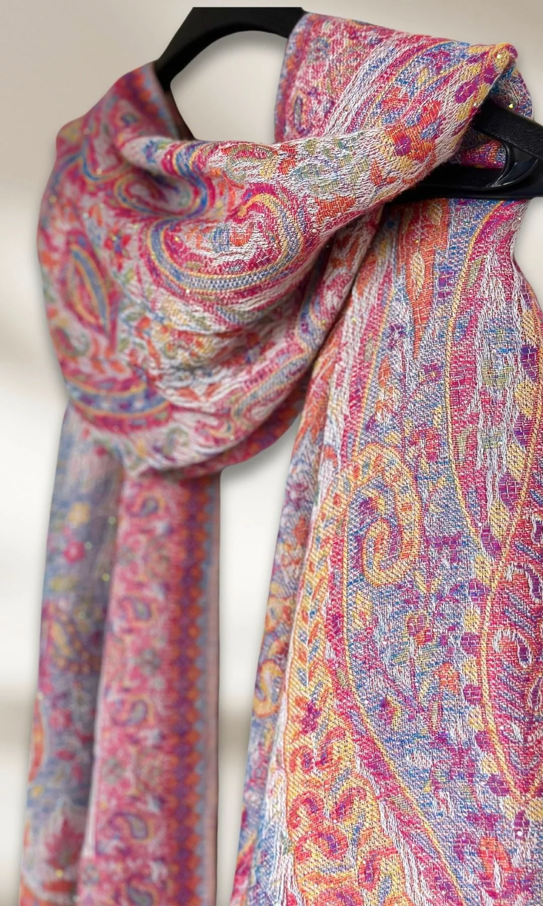 Close up look at the pink multi-colored pashmina scarf shawl with details of blue, yellow, pink, purple, and orange. Topped with small iridescent rainbow sparkling gems. Fringe color is white.
