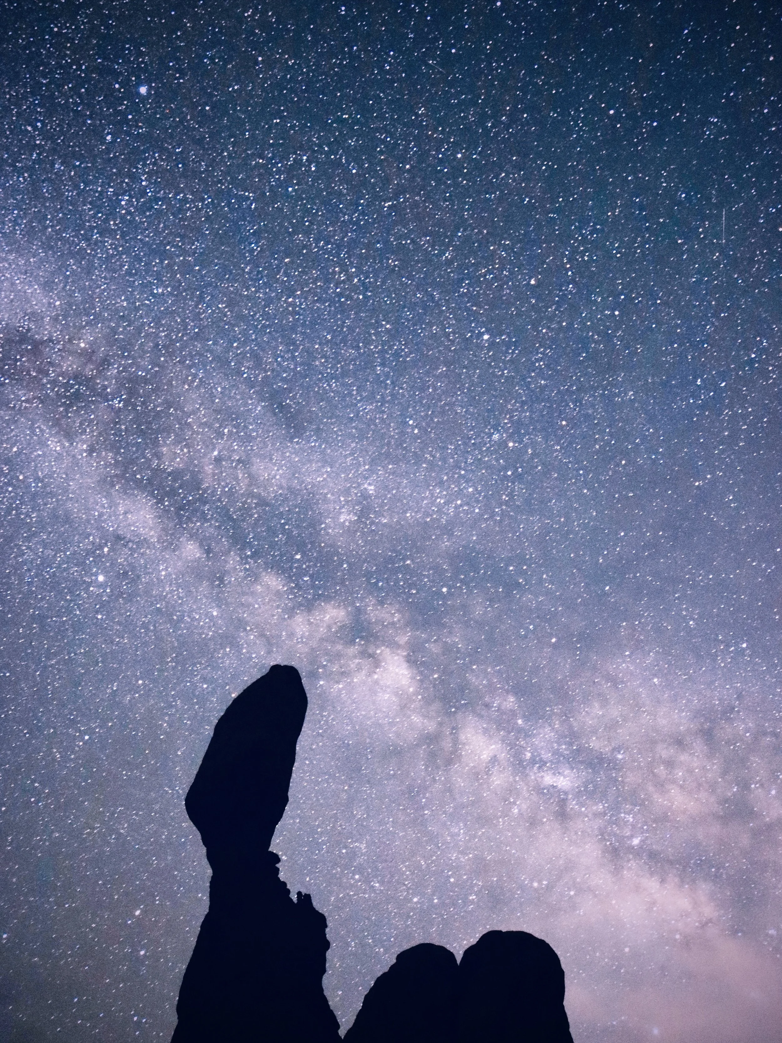 Silhouette of a person standing on rocky terrain at night, looking up at a star-filled sky with the Milky Way galaxy visible.
