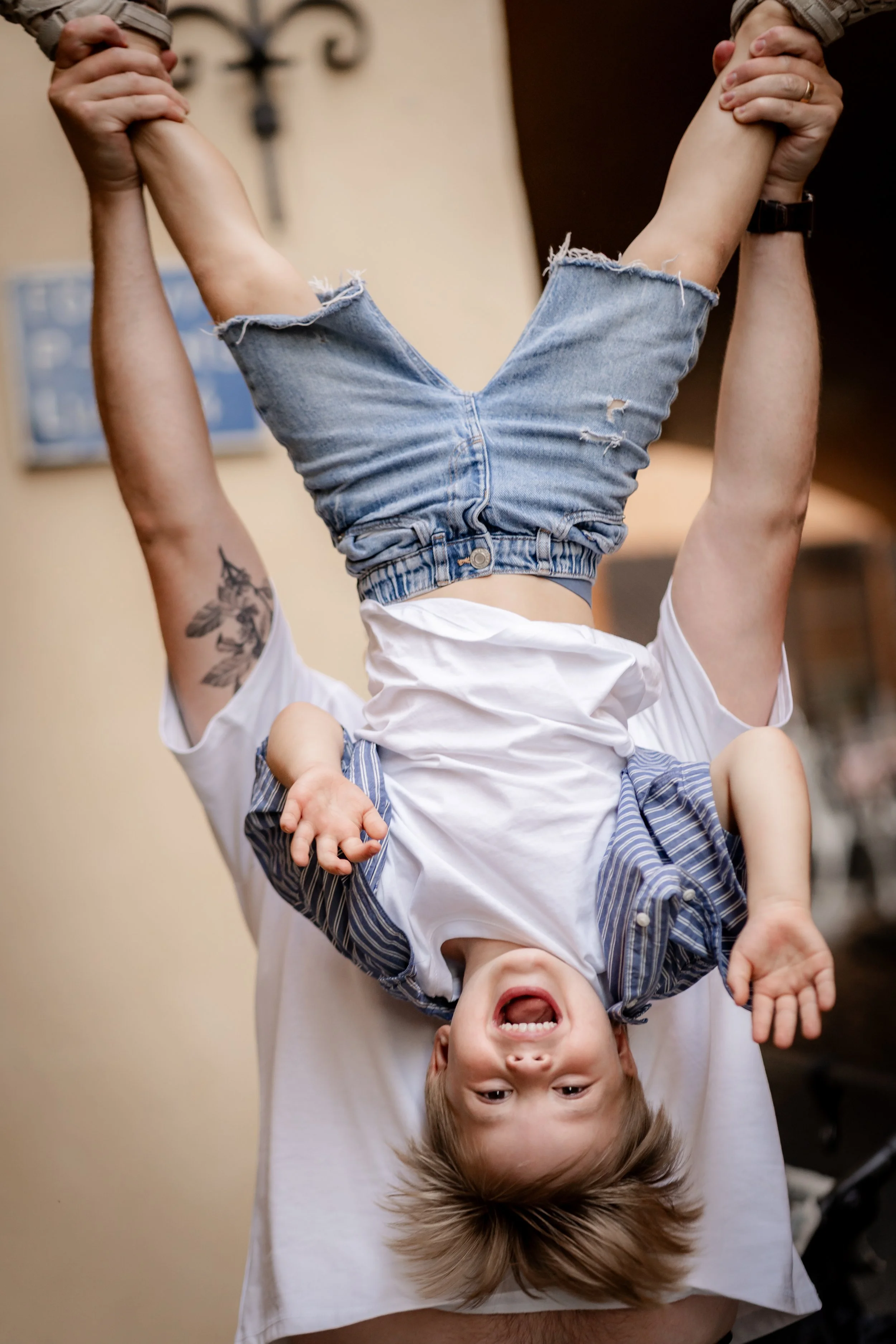 A child upside down with arms flailing, being held by an adult.