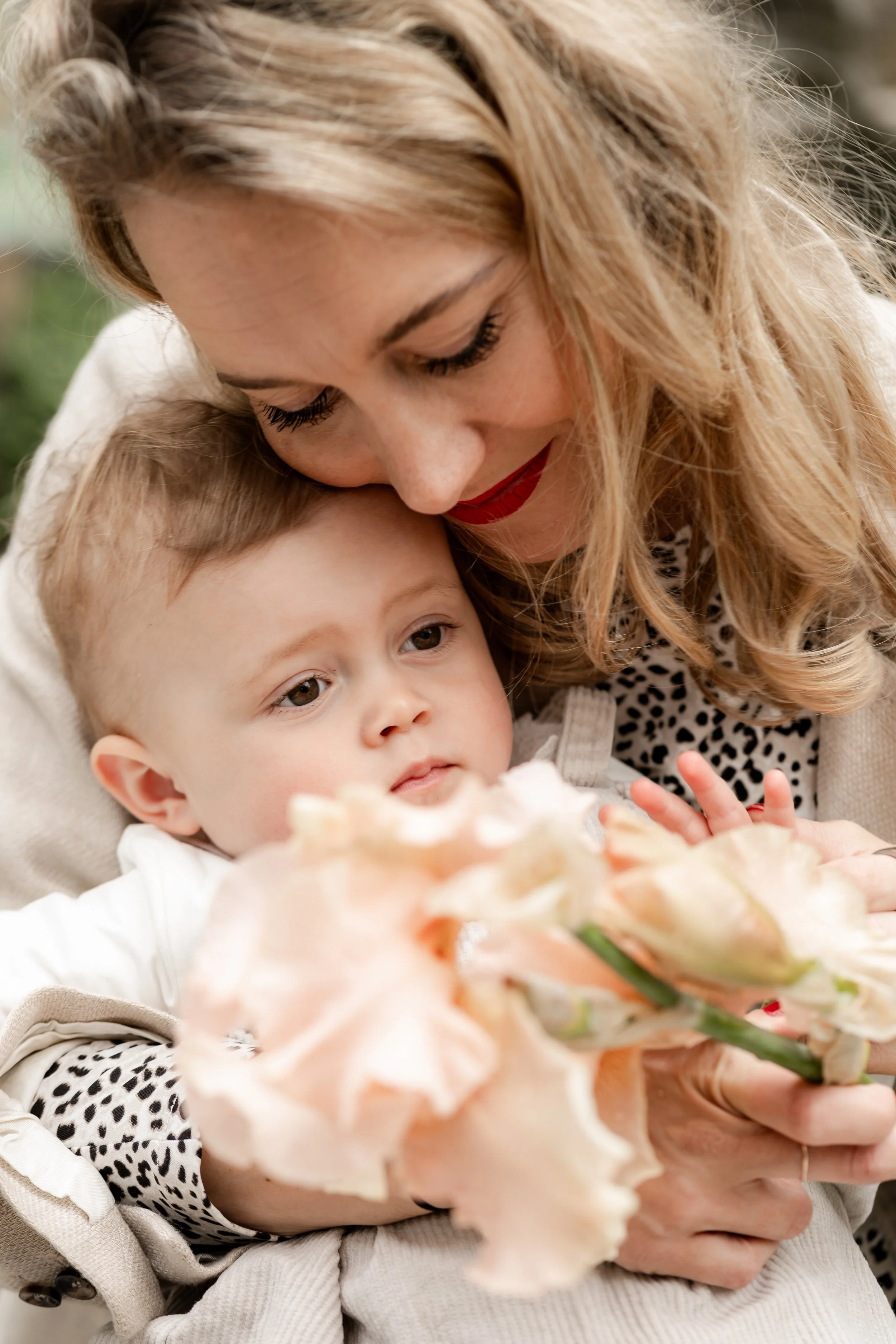 A woman lovingly holding a young boy and presenting flowers in an outdoor setting.