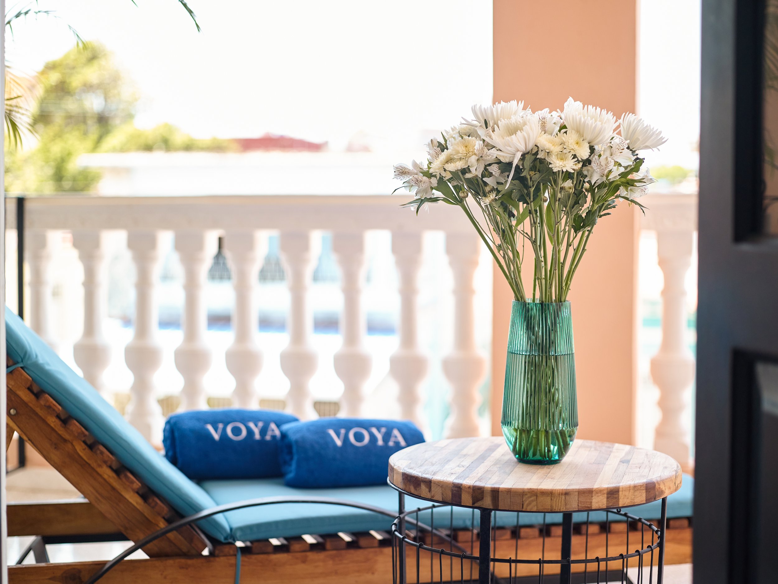 Balcony at VOYA Boutique Hotel Havana with tropical flowers, lounge chair, and blue towels overlooking colonial railings.