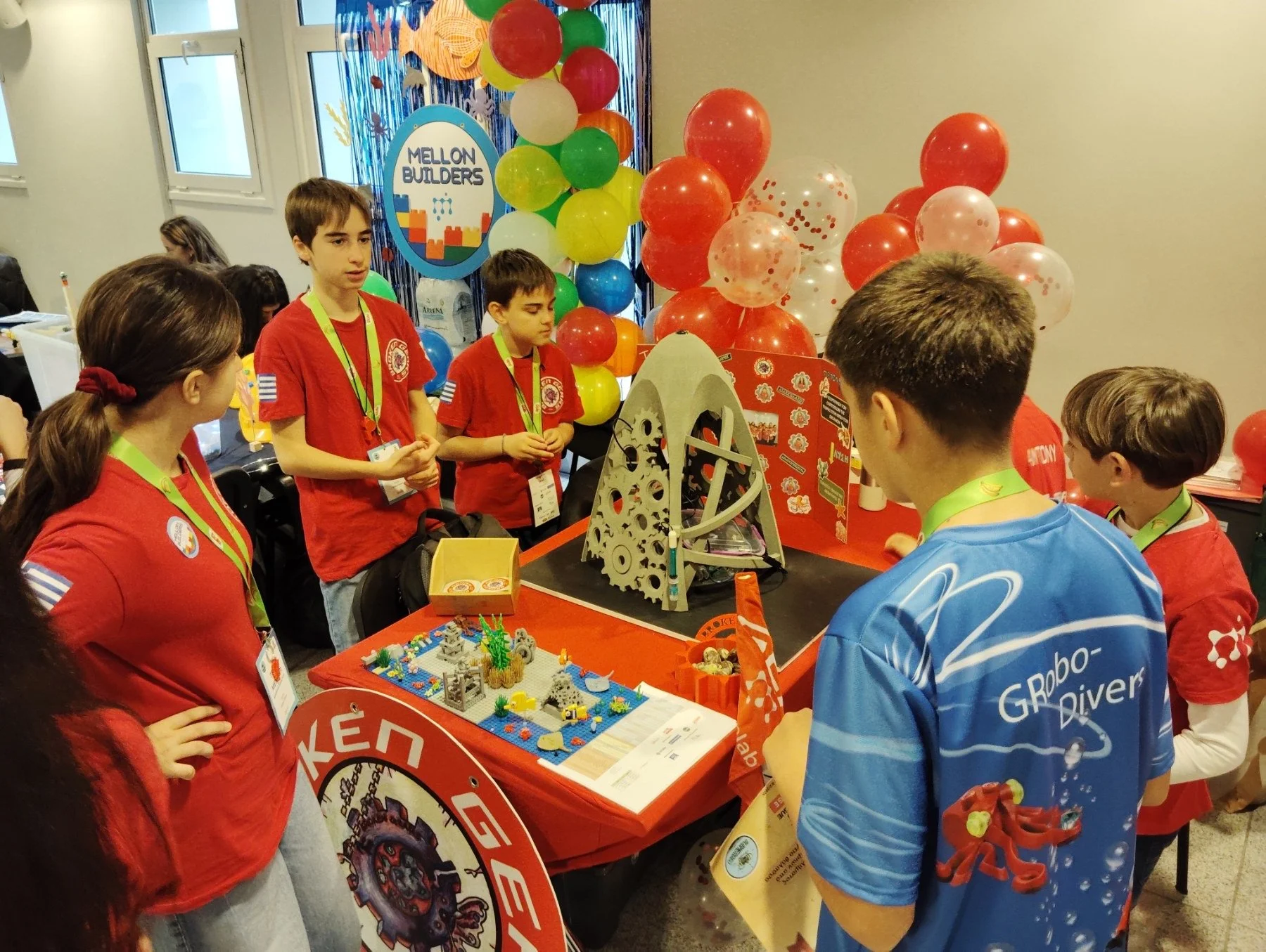 A group of children at a robotics exhibition showing a mechanical robot and LEGO creations, with colorful balloons in the background.