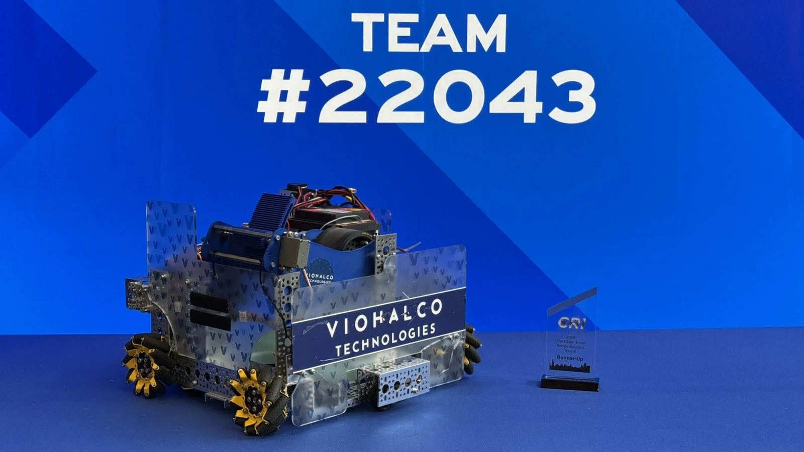 Το αγωνιστικό ρομπότ της ομάδας FTC VIOHALCO TECHNOLOGIES #22043 του MellonLab δίπλα στο Clark Street Bridge Builders Award και την ελληνική σημαία στο Chicago Robotics Invitational 2026.