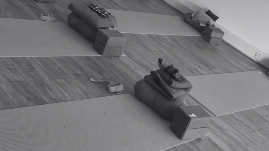 Yoga mats, blankets, and blocks arranged in a room with hardwood floors.