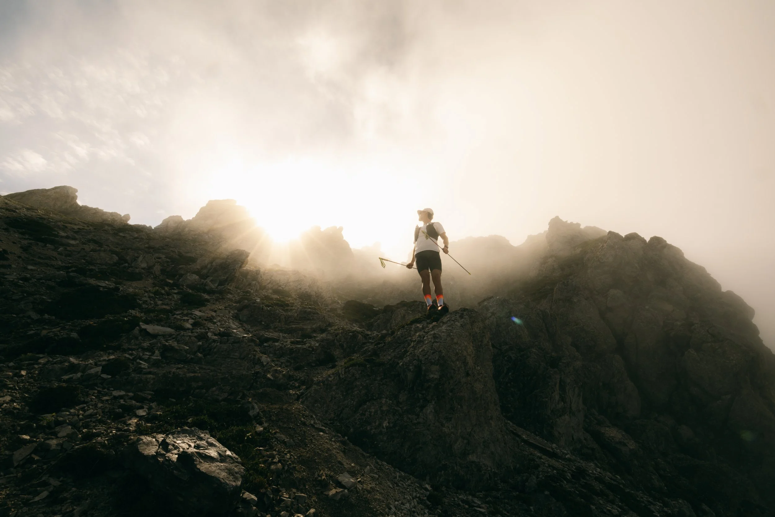 Eine Person beim Wandern in den Bergen bei Sonnenaufgang oder Sonnenuntergang, mit Blick auf den Himmel und umgebende Felsen.